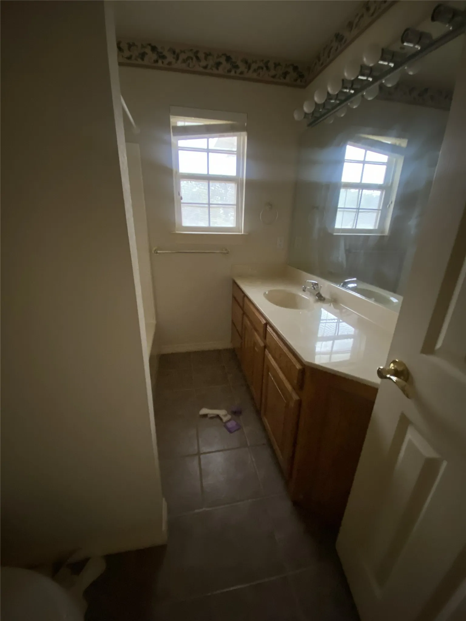 Dual window vanity area with a light-toned countertop, wood-finish cabinetry, and tiled flooring