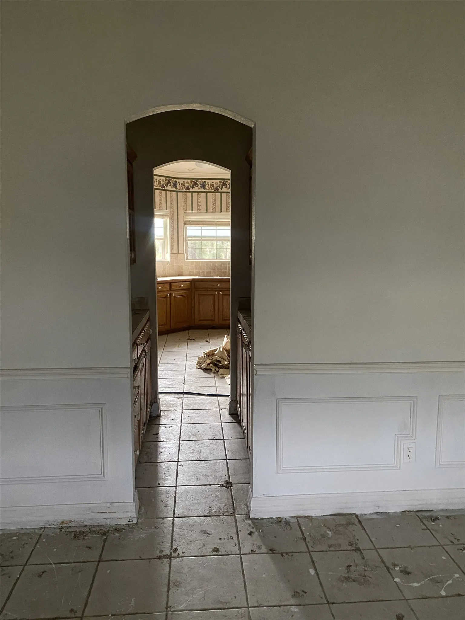 Arched doorway leading to a kitchen with wood-finish cabinetry, a tiled backsplash, and natural light