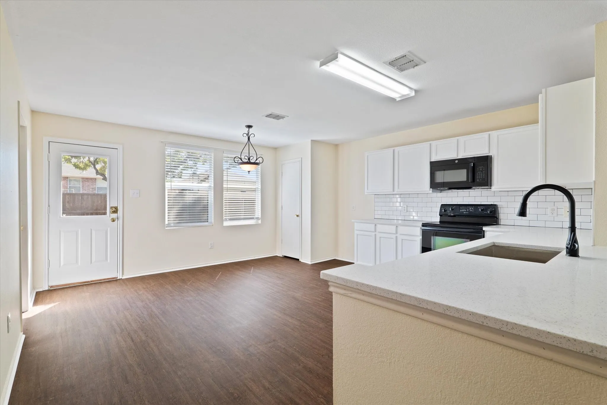 Kitchen featuring tasteful backsplash, black appliances, light stone countertops, white cabinetry, and dark wood-style floors