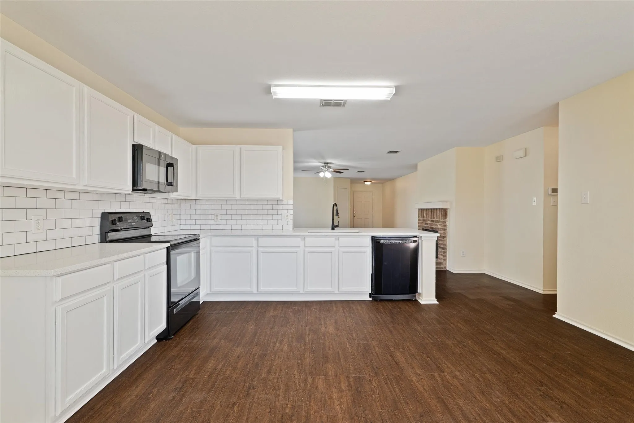 Kitchen with black appliances, backsplash, a peninsula, white cabinets, and dark wood-type flooring