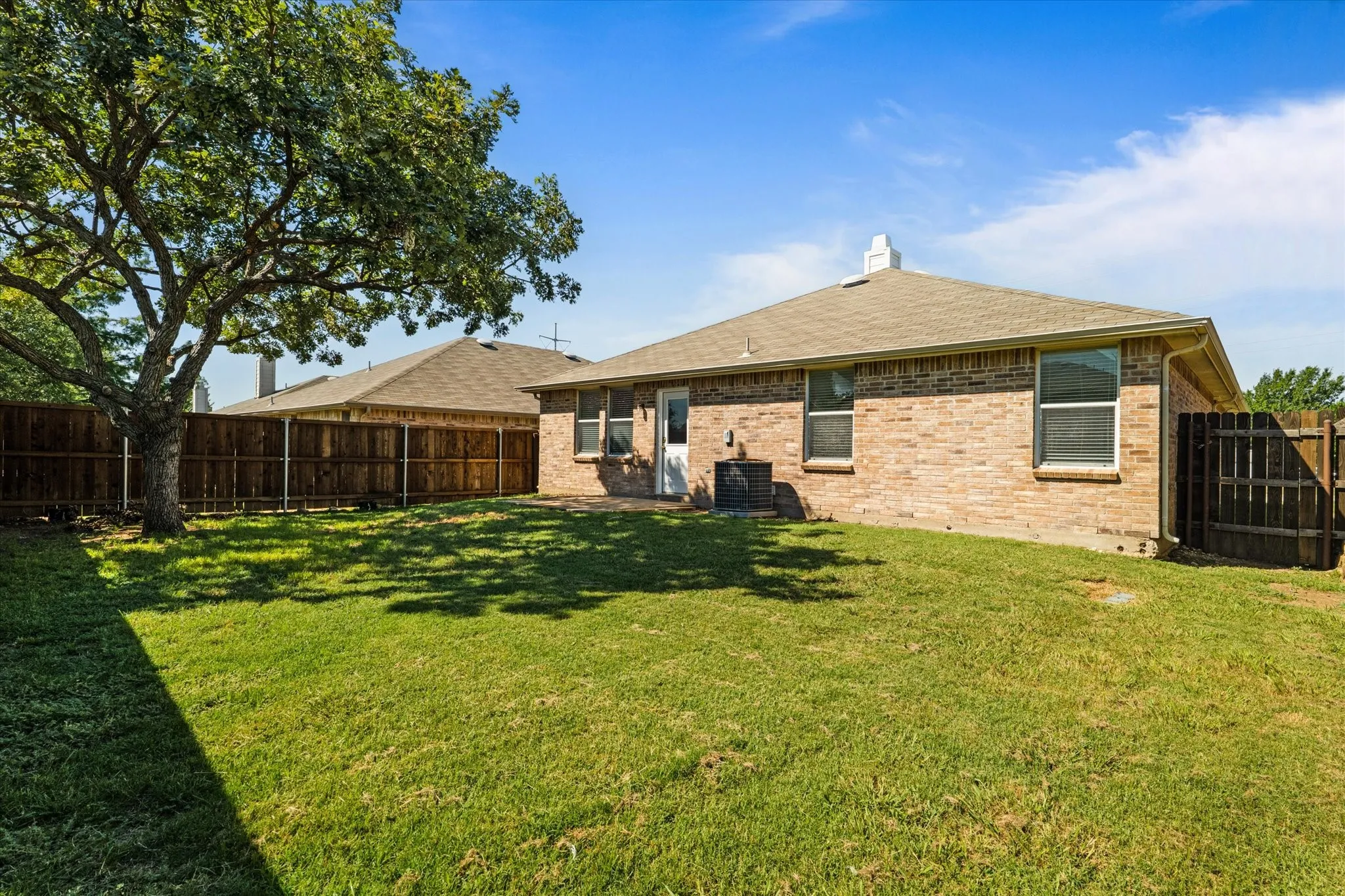 Back of house with brick siding, roof with shingles, a fenced backyard, and a chimney