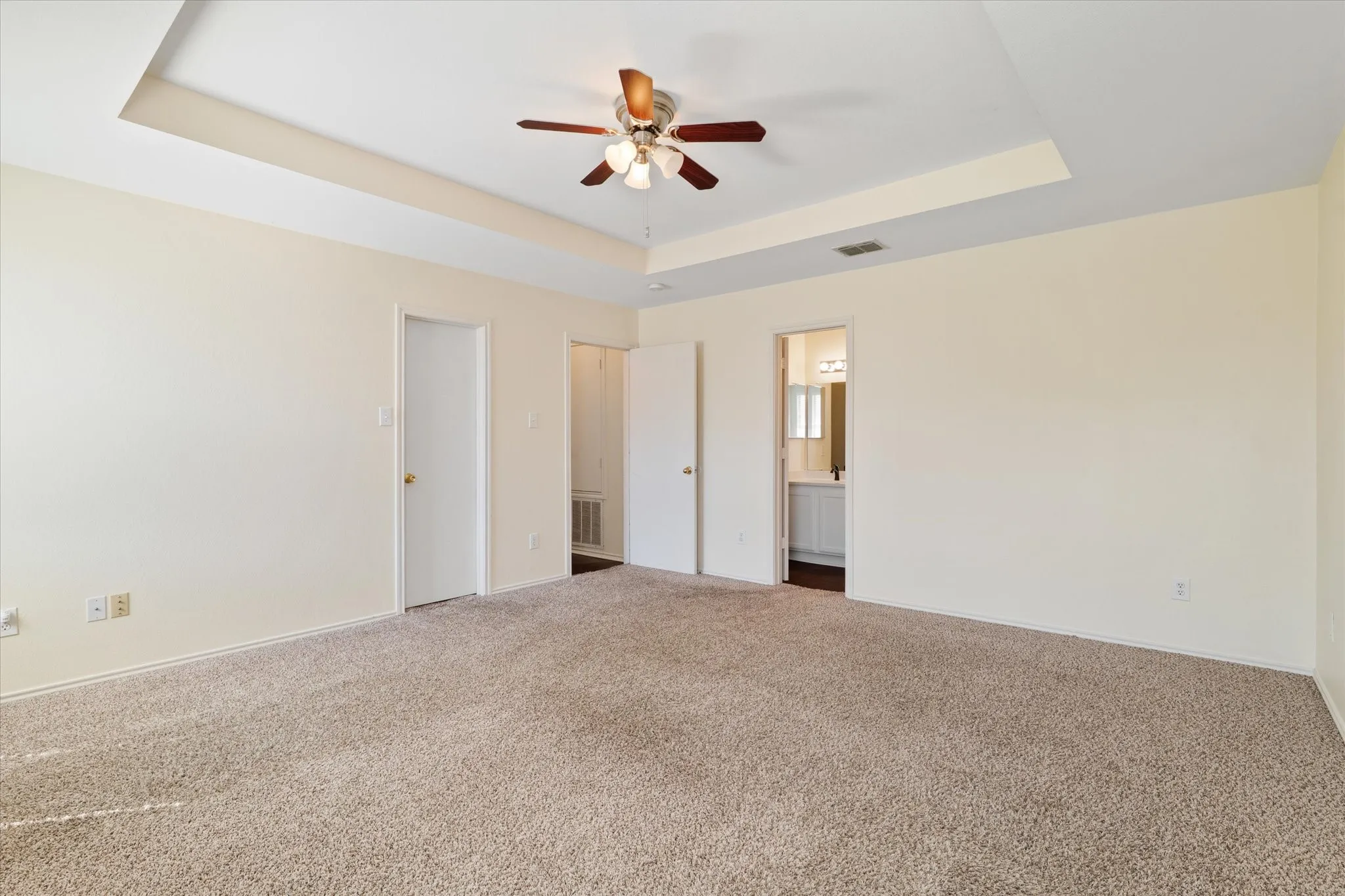 Unfurnished bedroom with a raised ceiling, carpet, connected bathroom, and ceiling fan