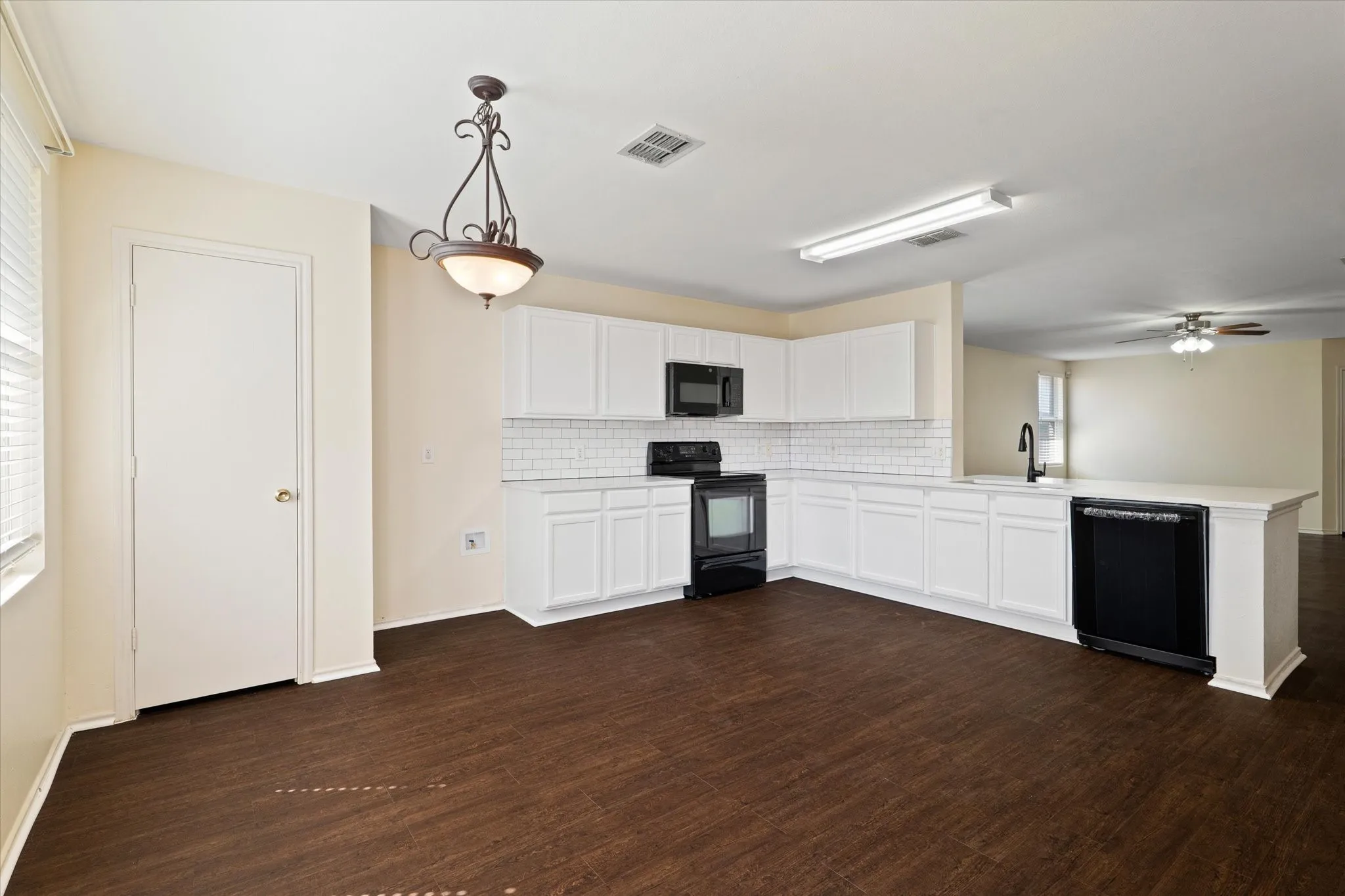 Kitchen with backsplash, a peninsula, black appliances, light countertops, and dark wood-type flooring