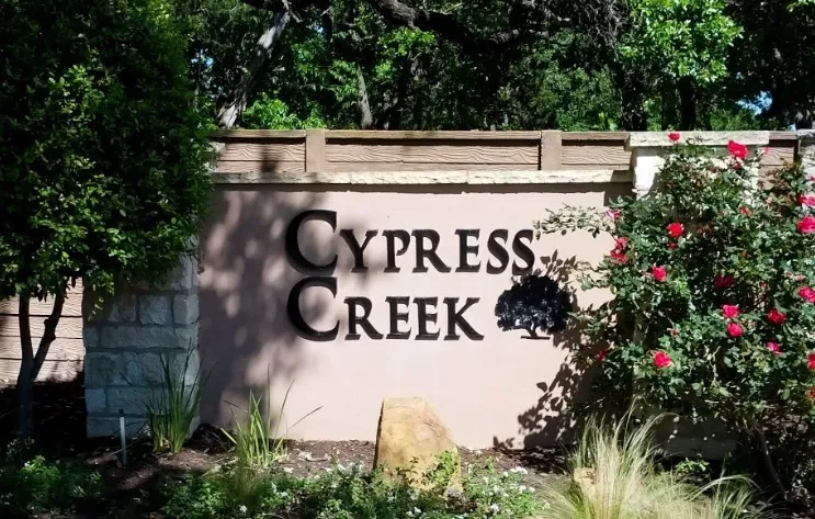 Cypress Creek community entrance featuring a stone and stucco monument sign, framed by mature trees and vibrant red flowering shrubs