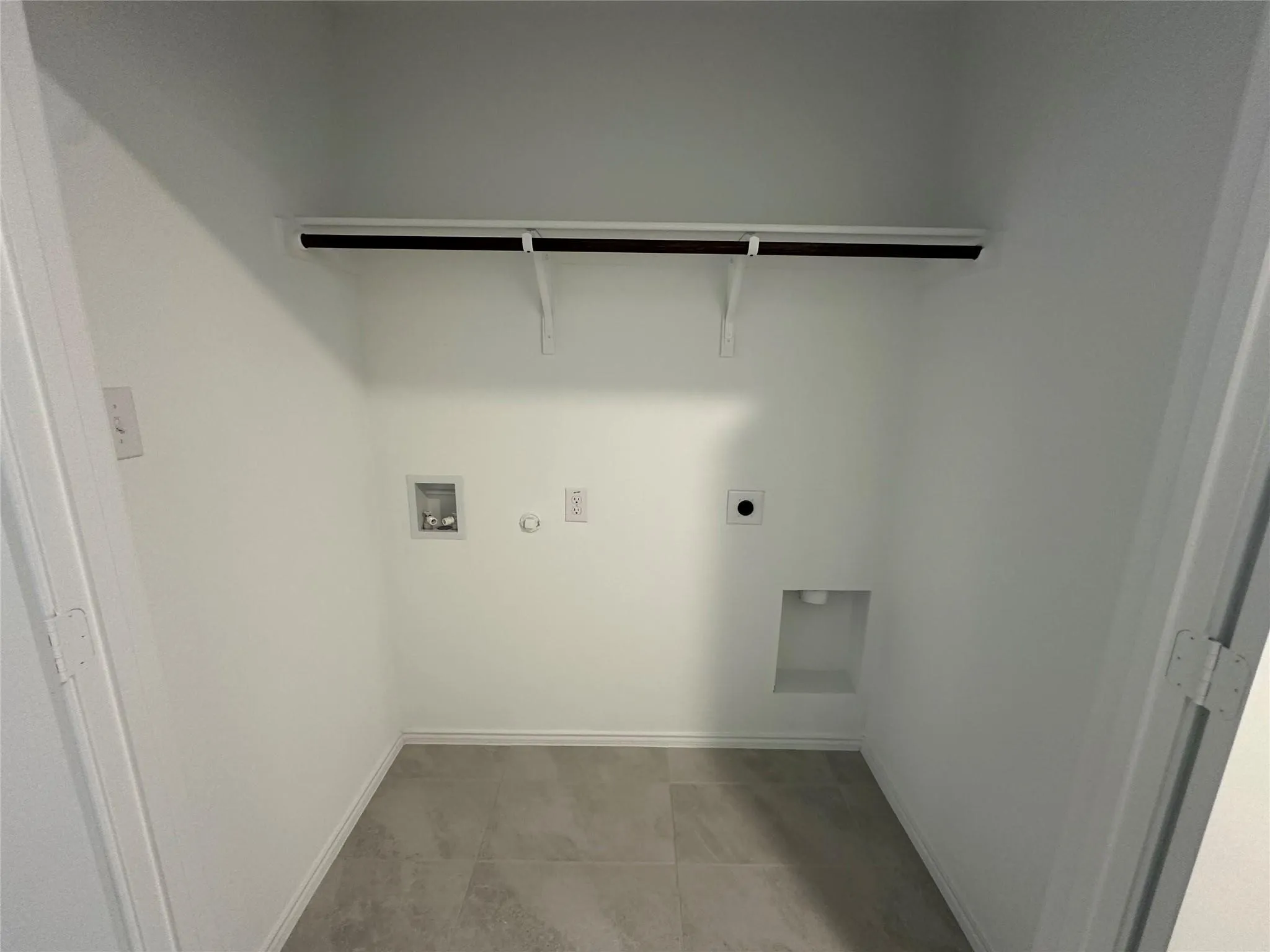 Dedicated utility space featuring light-toned tile flooring, white walls, built-in shelving, washer hookups, and dryer hookups