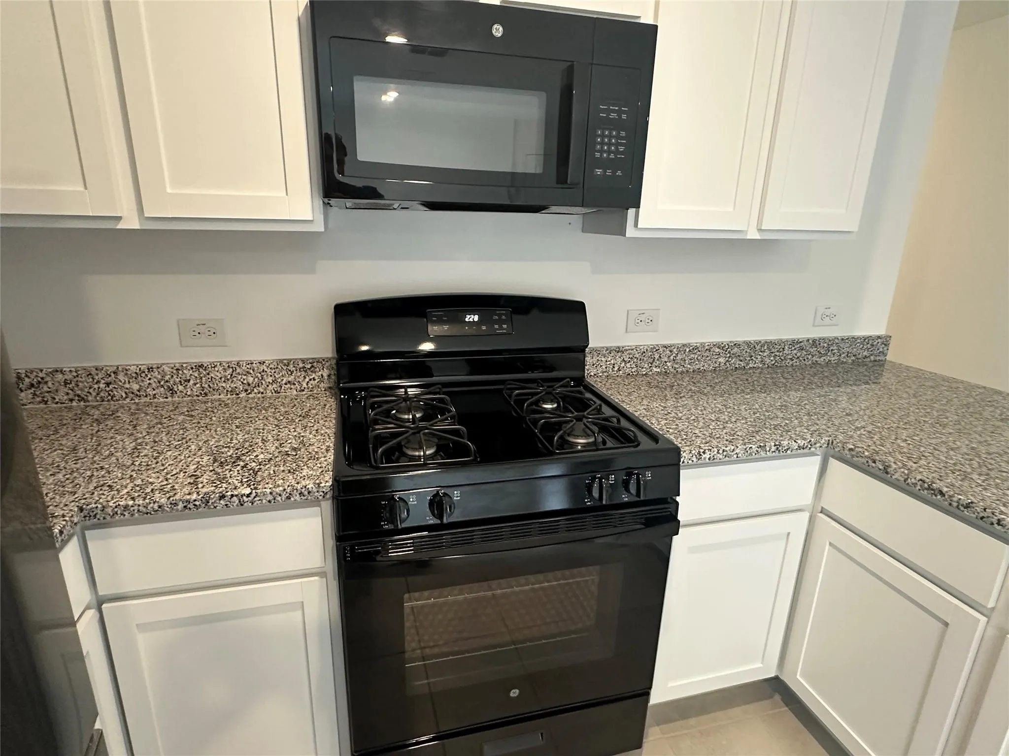 Kitchen featuring a black gas range with an overhead microwave, white cabinetry, and speckled countertops