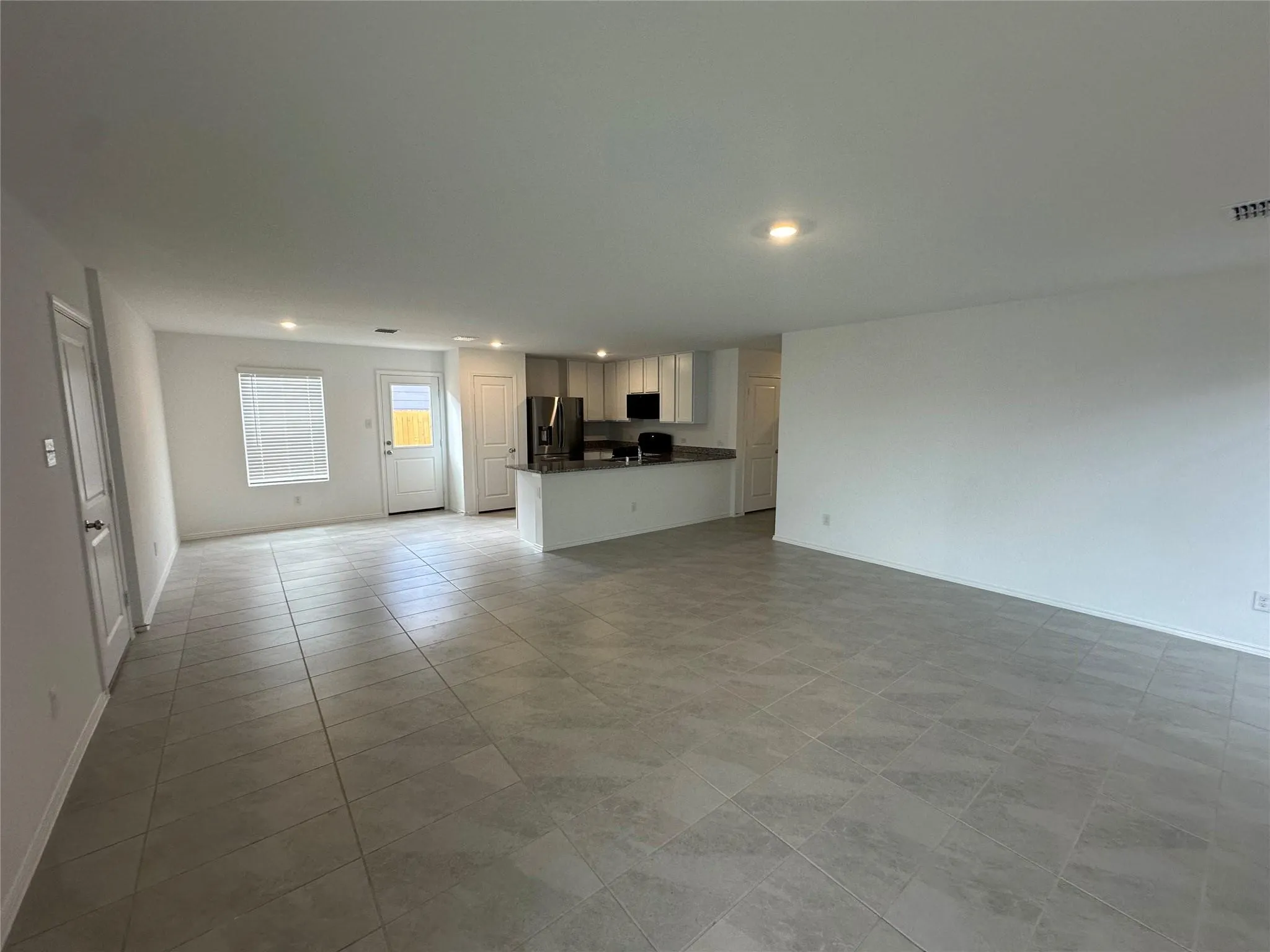 Spacious open concept living area featuring large format tile flooring, recessed lighting, a kitchen with light-colored cabinetry, a breakfast bar, and a stainless steel refrigerator