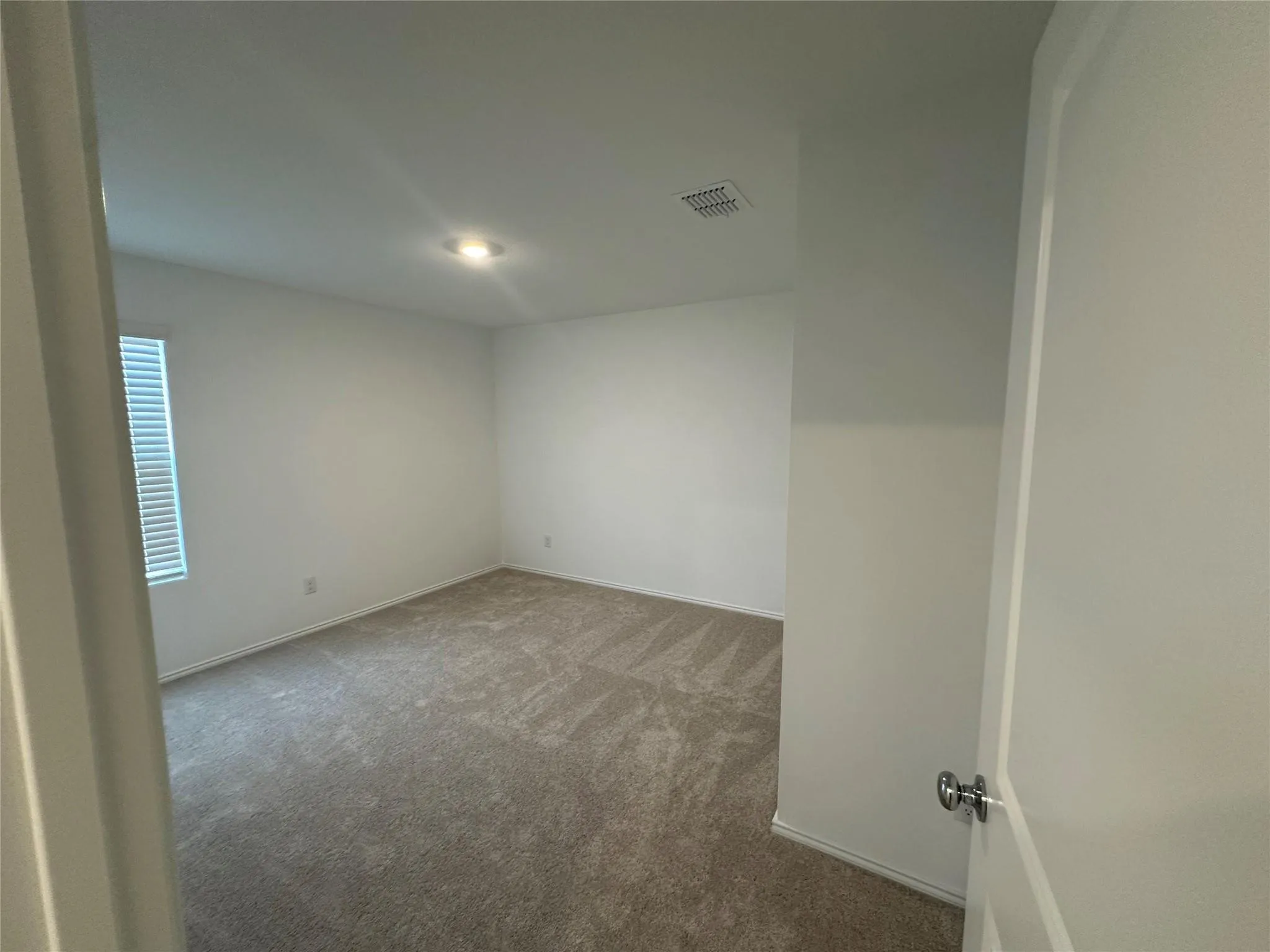 Carpeted room with white walls, a single recessed ceiling light fixture, and a window with horizontal blinds