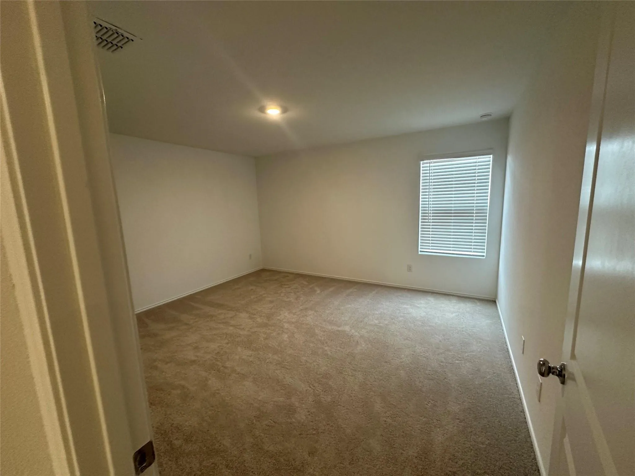 Spacious room featuring neutral carpet flooring, white walls, a single window with blinds, and a ceiling-mounted light fixture