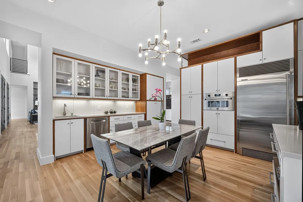 Anchored by a contemporary chandelier, white oak floors, and custom cabinetry, this dining area sits directly inside the downstairs kitchen