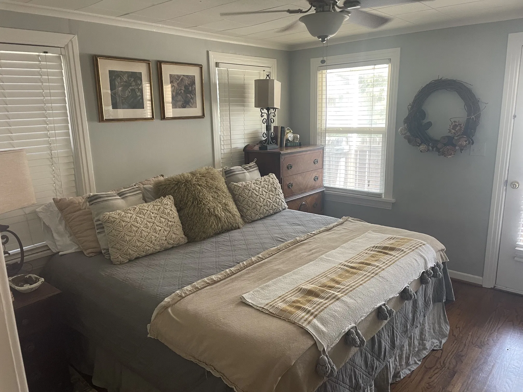 Hardwood-style flooring, ceiling fan with light fixture, multiple windows with blinds, light gray wall color, paneled ceiling