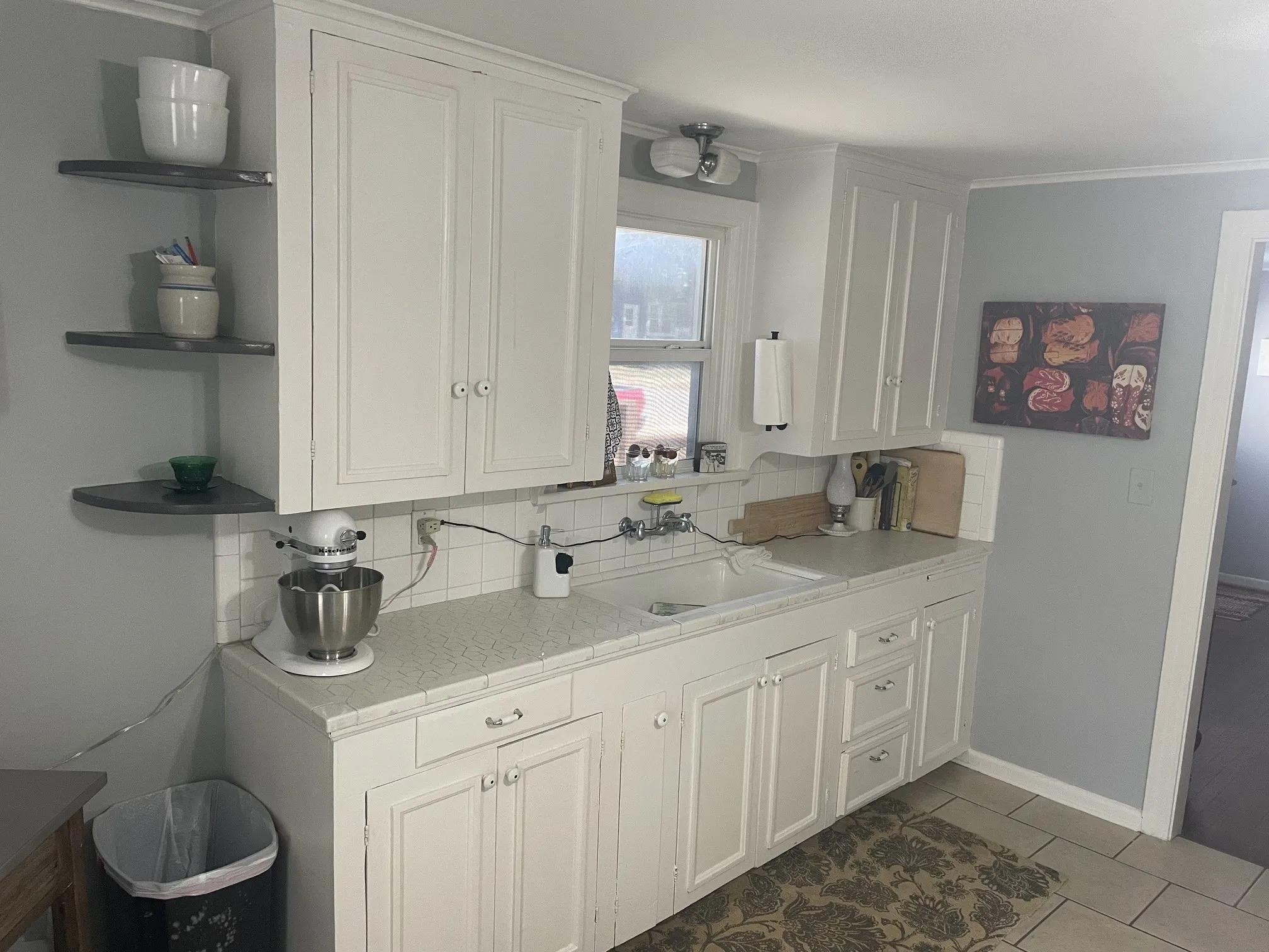 White cabinetry with recessed panel doors, corner floating shelves, a tiled backsplash, and light-toned countertops