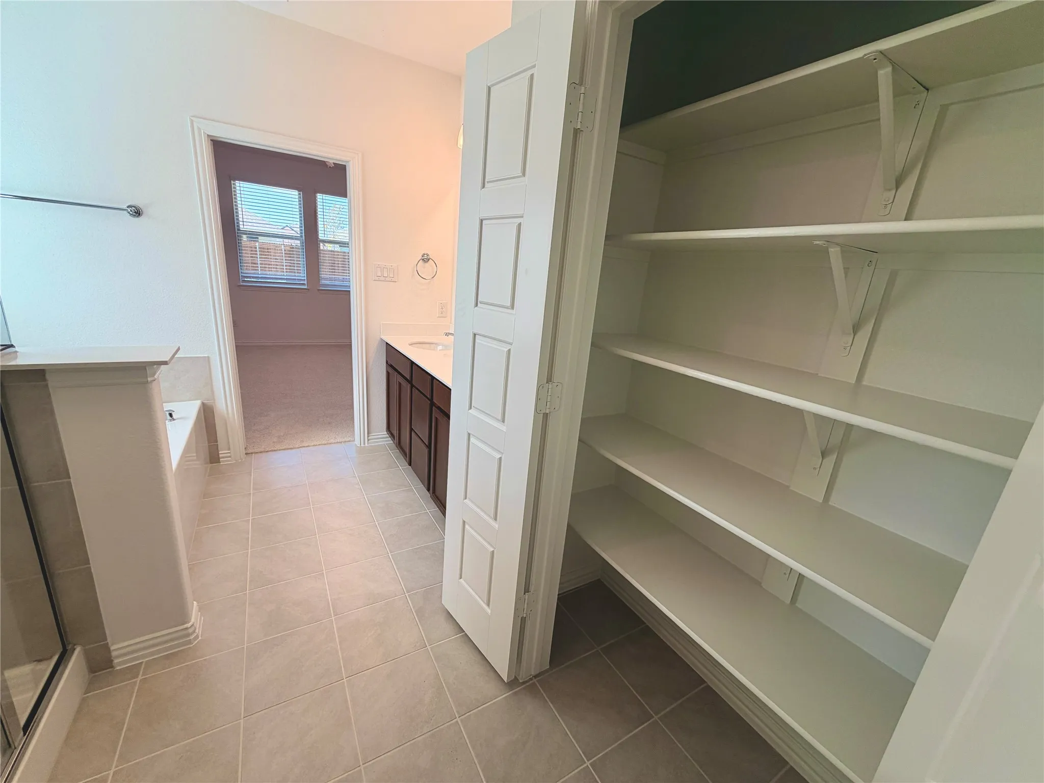 Tiled flooring, built-in bathtub, vanity with a single sink, dark wood-finish cabinetry, and built-in shelving
