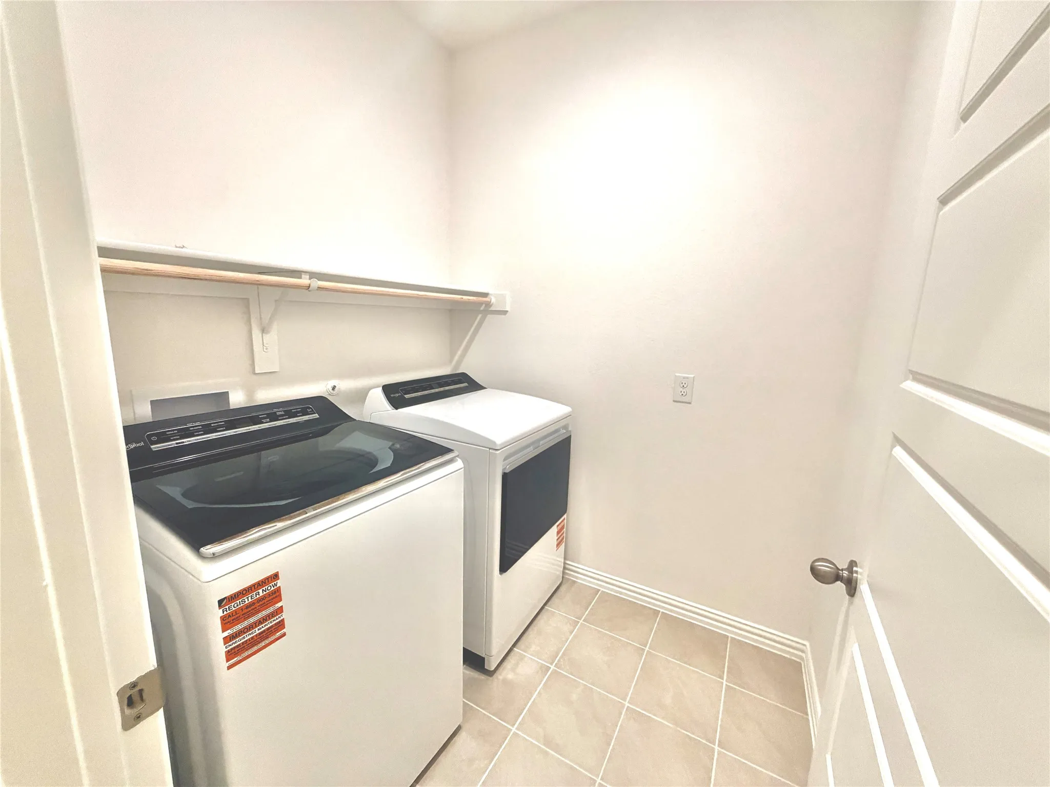 Utility area with light-colored tile flooring, overhead shelving, and a hanging rod