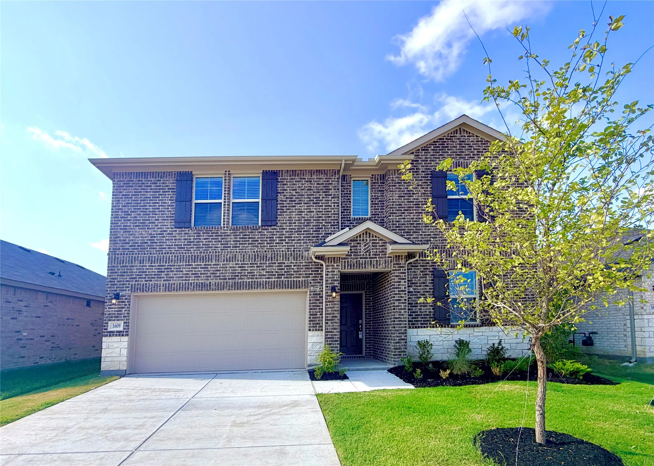Two-story brick exterior with stone accents, attached garage, covered entry, and manicured landscaping