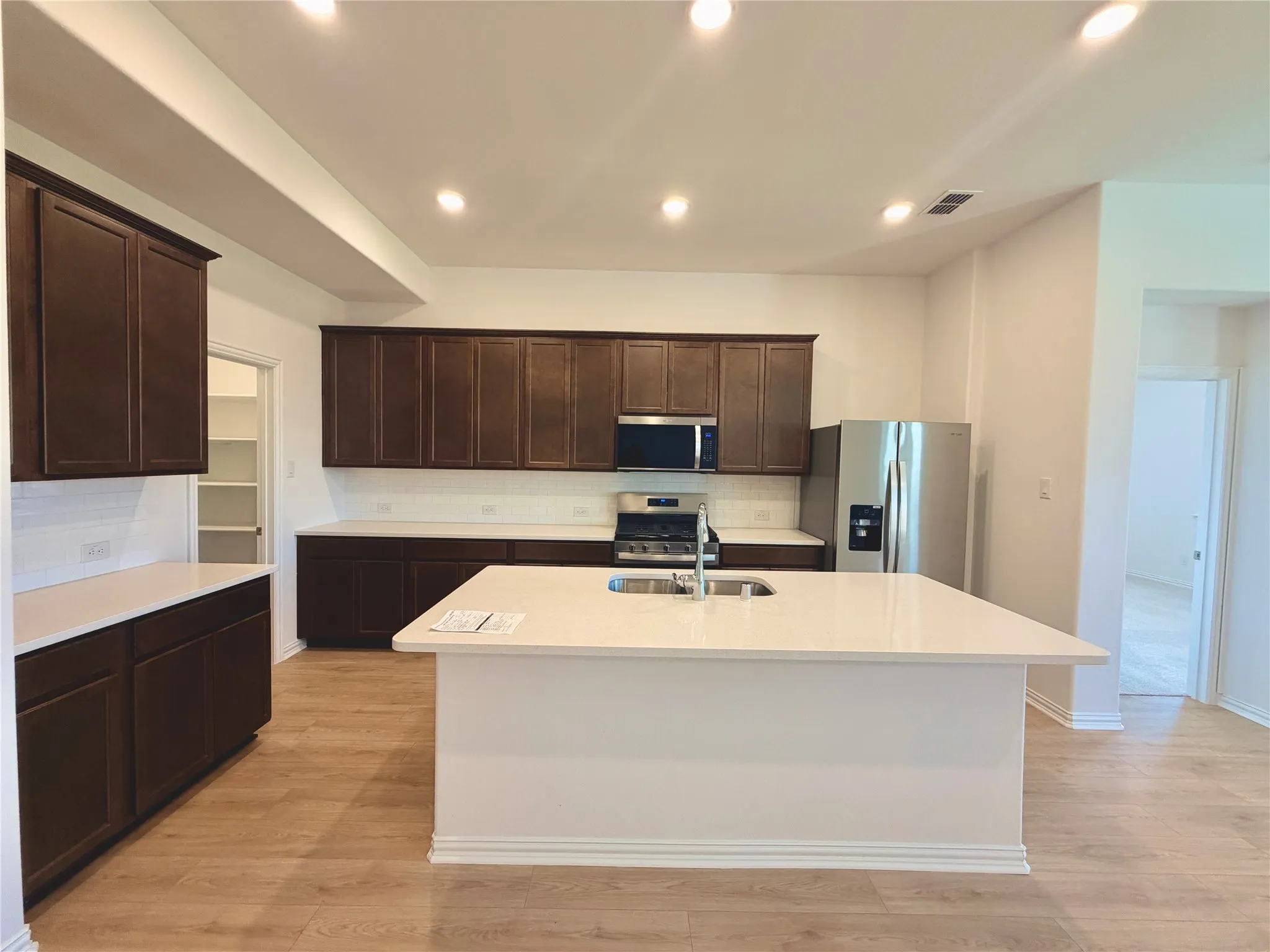 Spacious kitchen featuring an expansive island, dark wood-finish cabinetry, white countertops, and stainless steel appliances