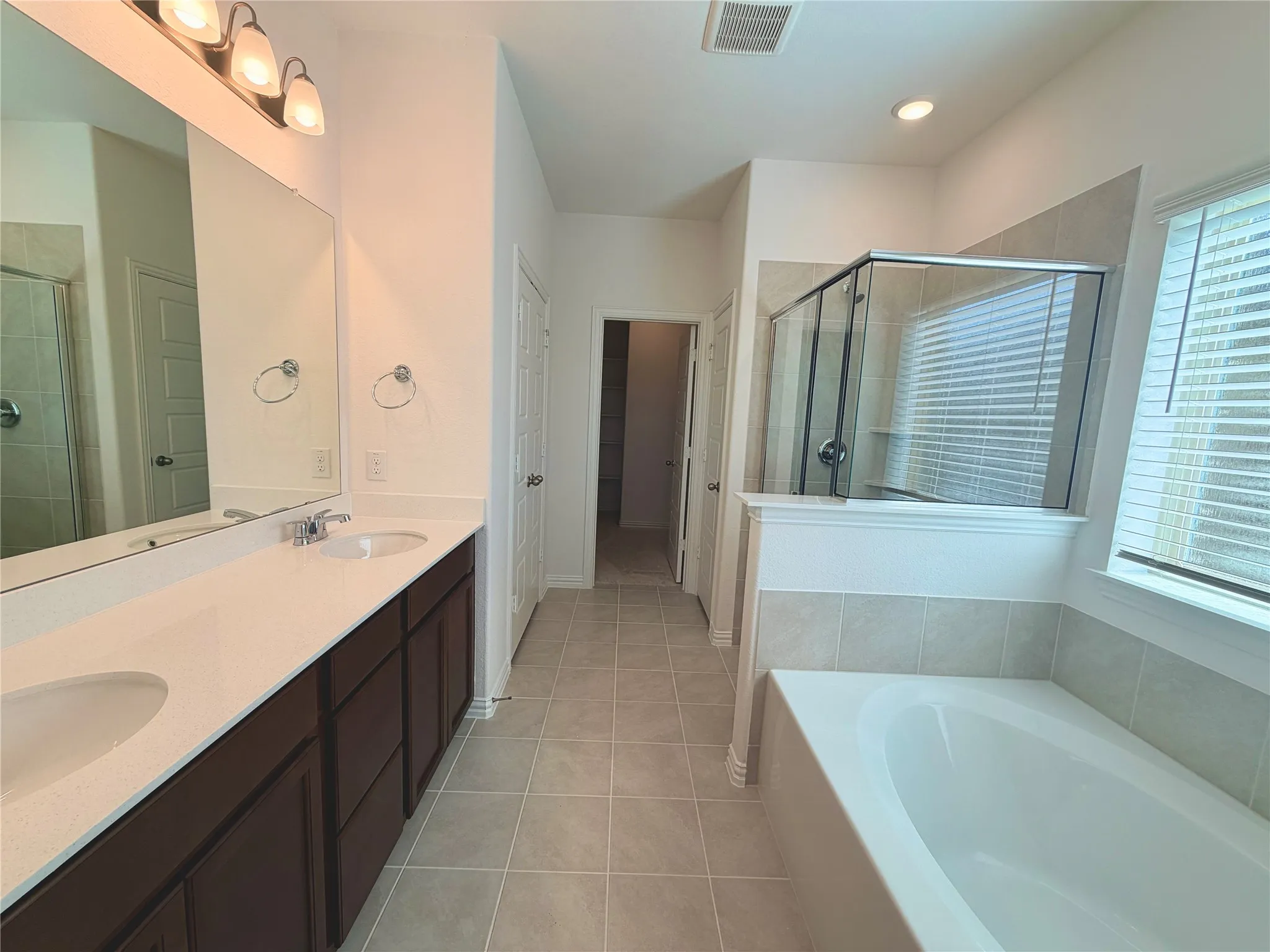 Bathroom with dual vanity, integrated sinks, dark wood-finish cabinetry, and a built-in tub with tile surround