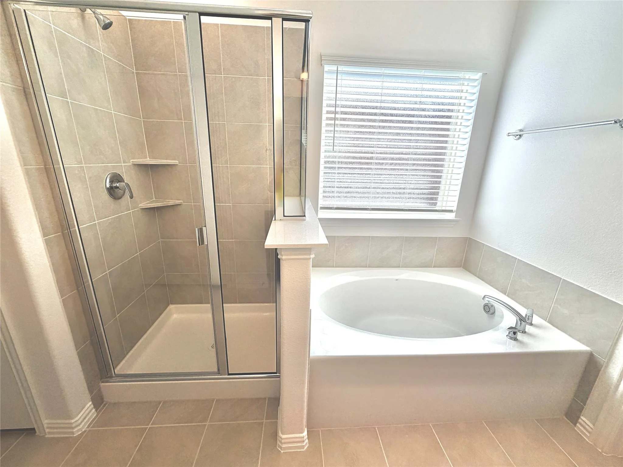 Tiled flooring complements the built-in garden tub and glass-enclosed shower with integrated shelving