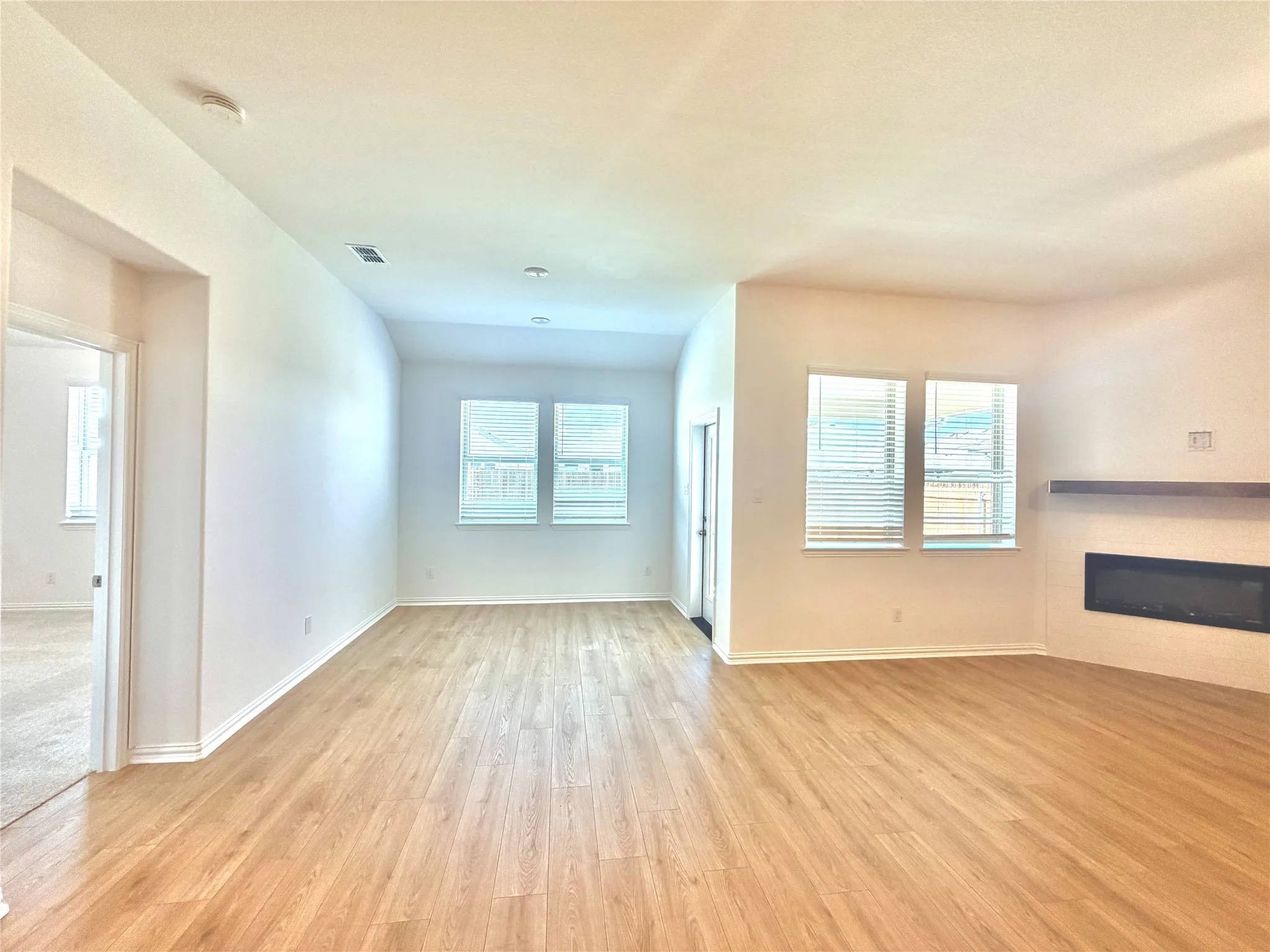 Wood-finish flooring throughout, multiple windows with blinds, built-in electric fireplace with stone-tile surround, and a floating wood mantel