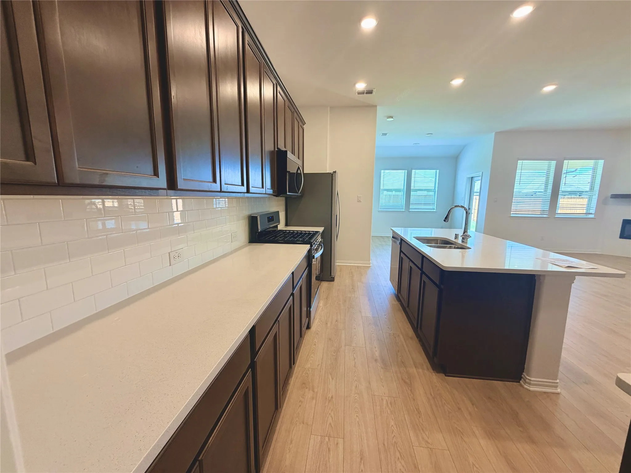 Open-concept kitchen featuring dark wood cabinetry, white subway tile backsplash, light-toned countertops, and wood-finish flooring