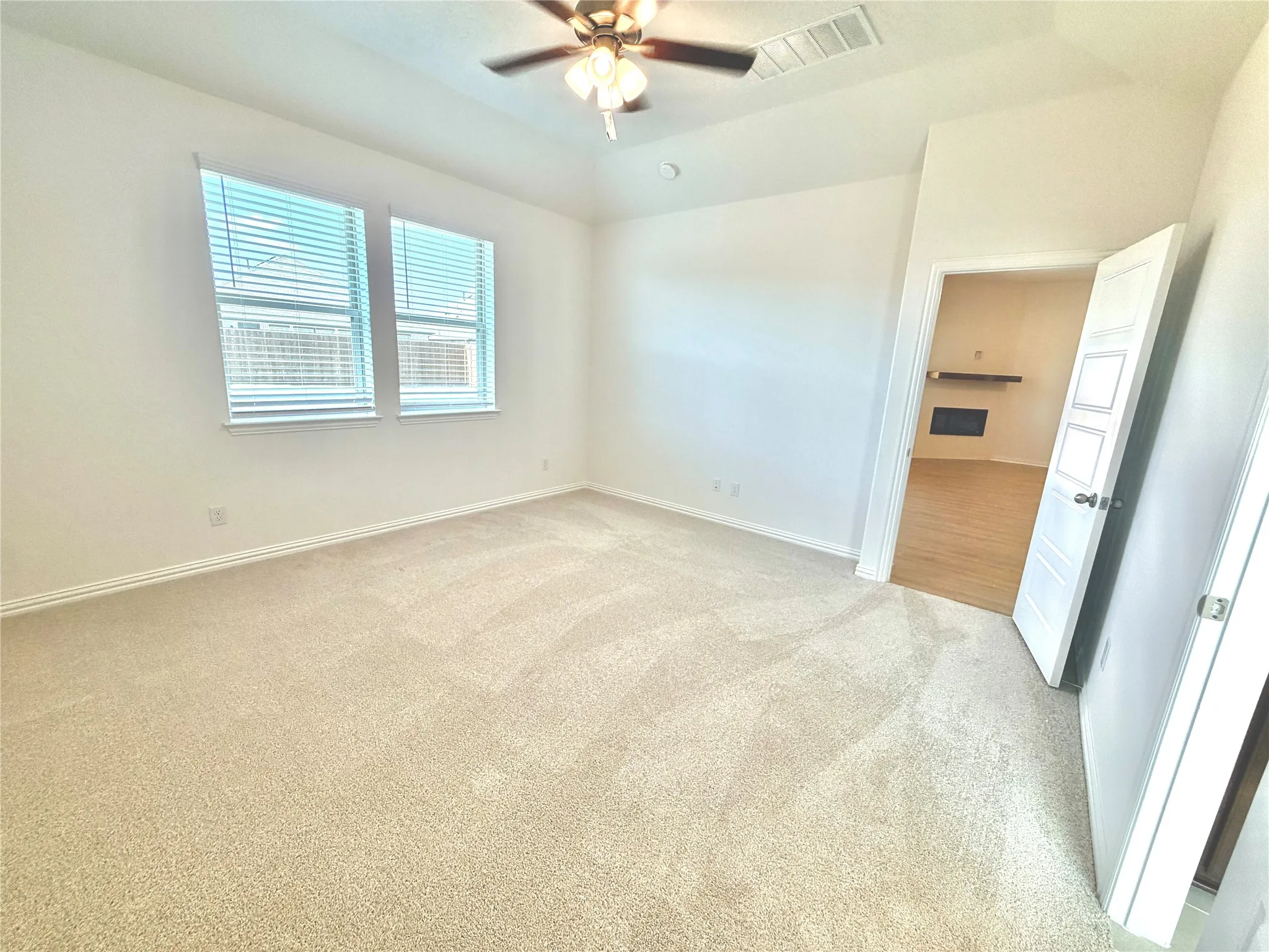 Plush carpeting throughout, two windows with blinds, ceiling fan with integrated lighting, and a paneled door