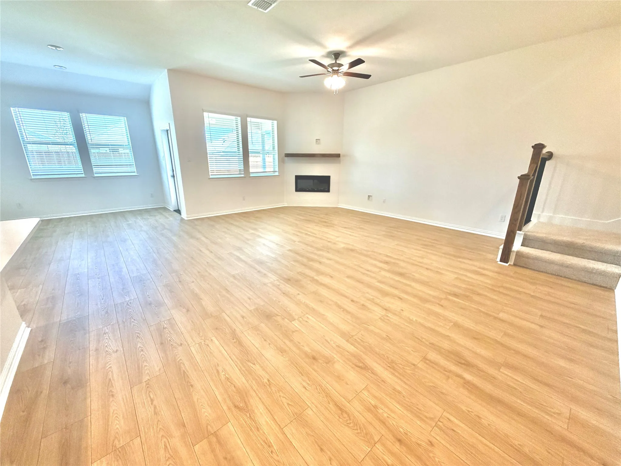 Spacious living area featuring wood-finish flooring, a built-in fireplace with a floating mantel, and multiple windows