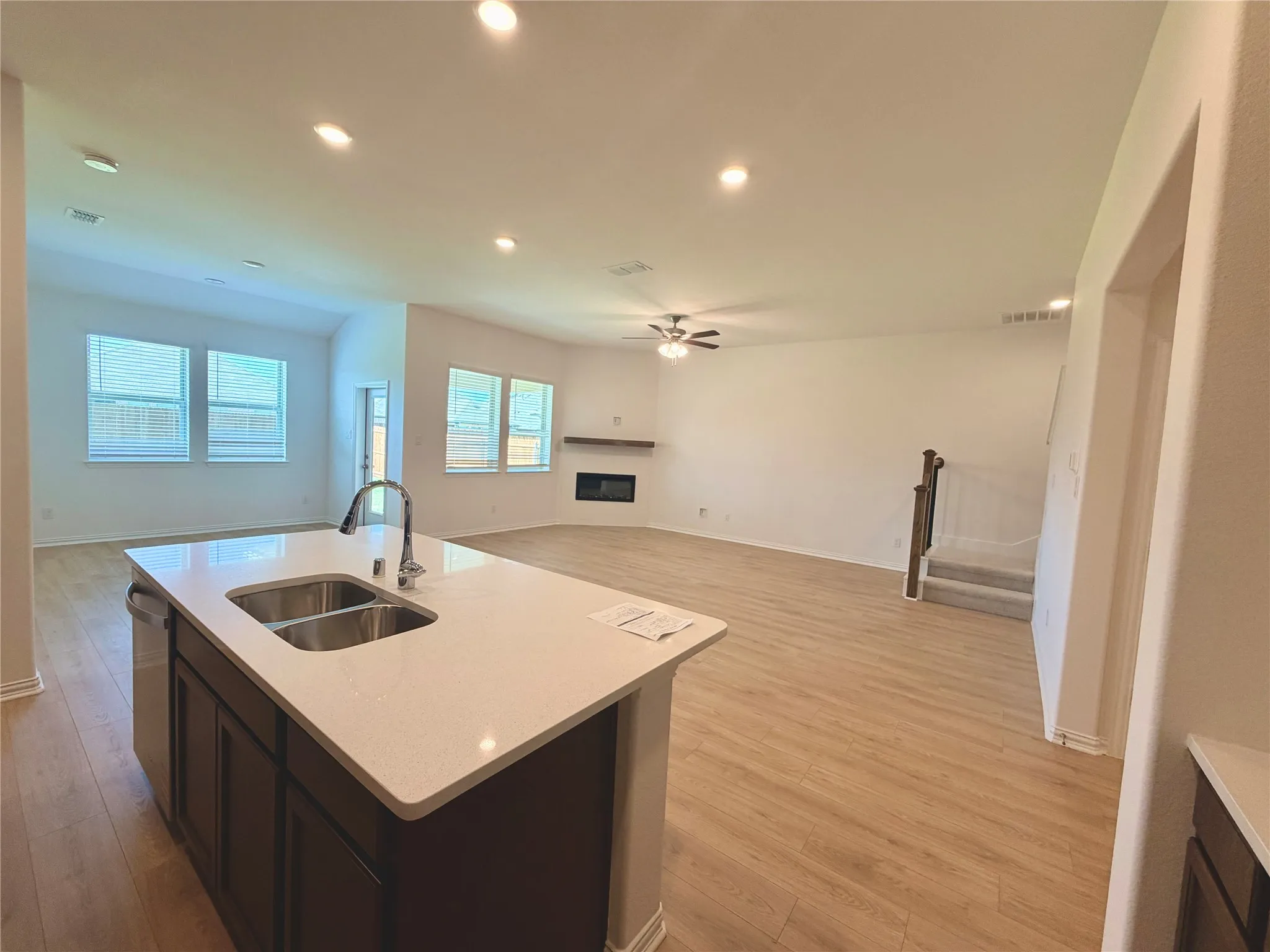 Spacious interior featuring wood-finish flooring, recessed lighting, and a kitchen island with an undermount double sink and quartz countertop