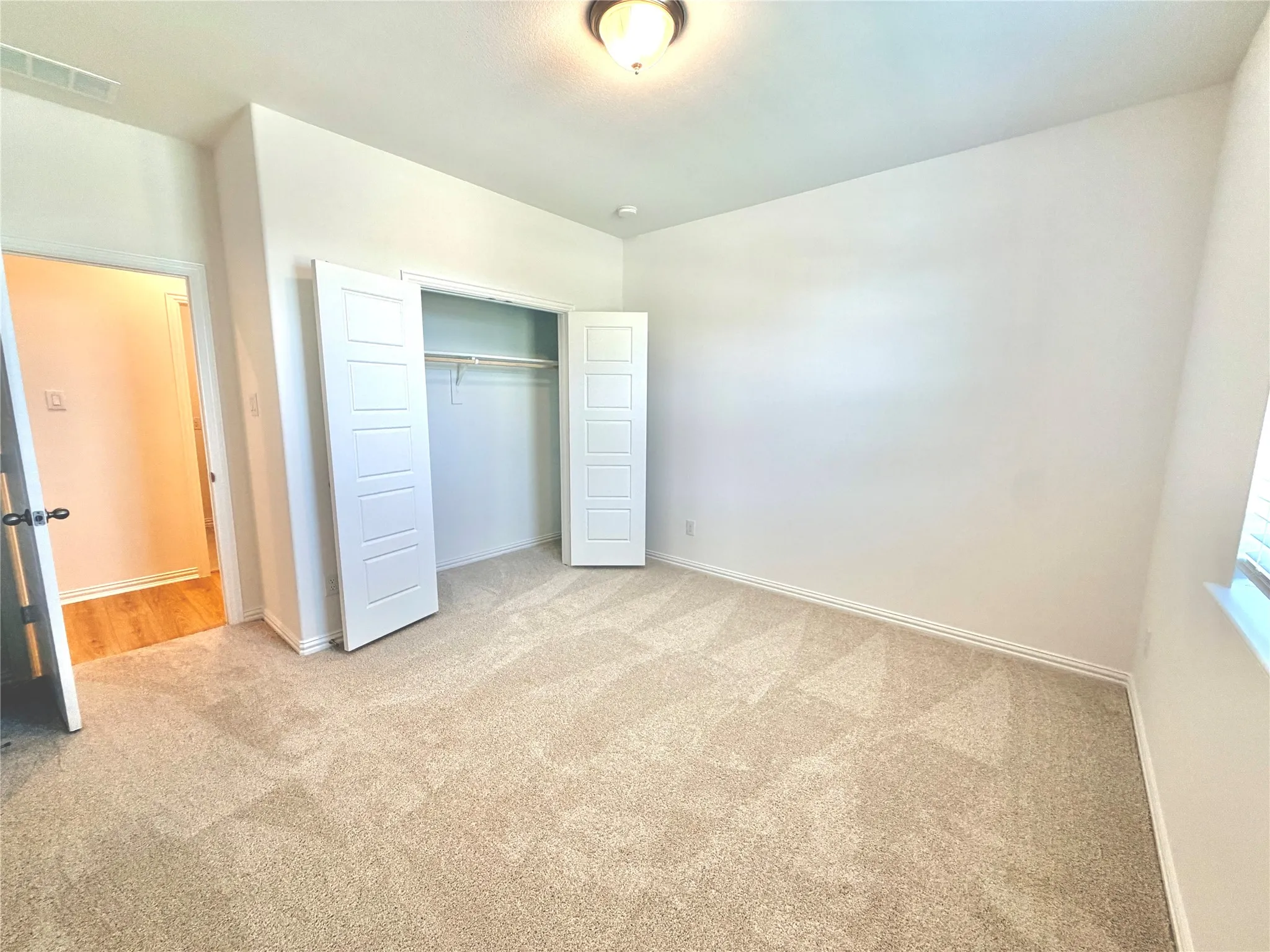 Neutral tone wall finishes, ceiling-mounted light fixture, carpeted flooring, window with blinds, and built-in closet with bifold doors