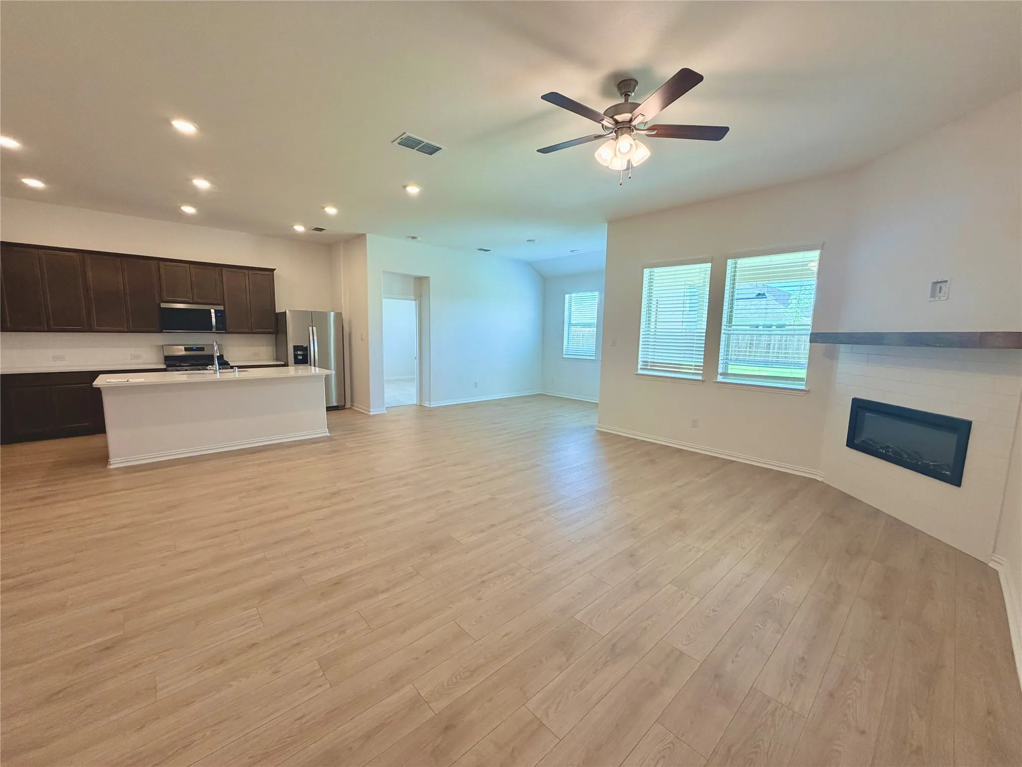Spacious living area featuring wood-finish flooring, a ceiling fan, and an electric fireplace with a wood mantel