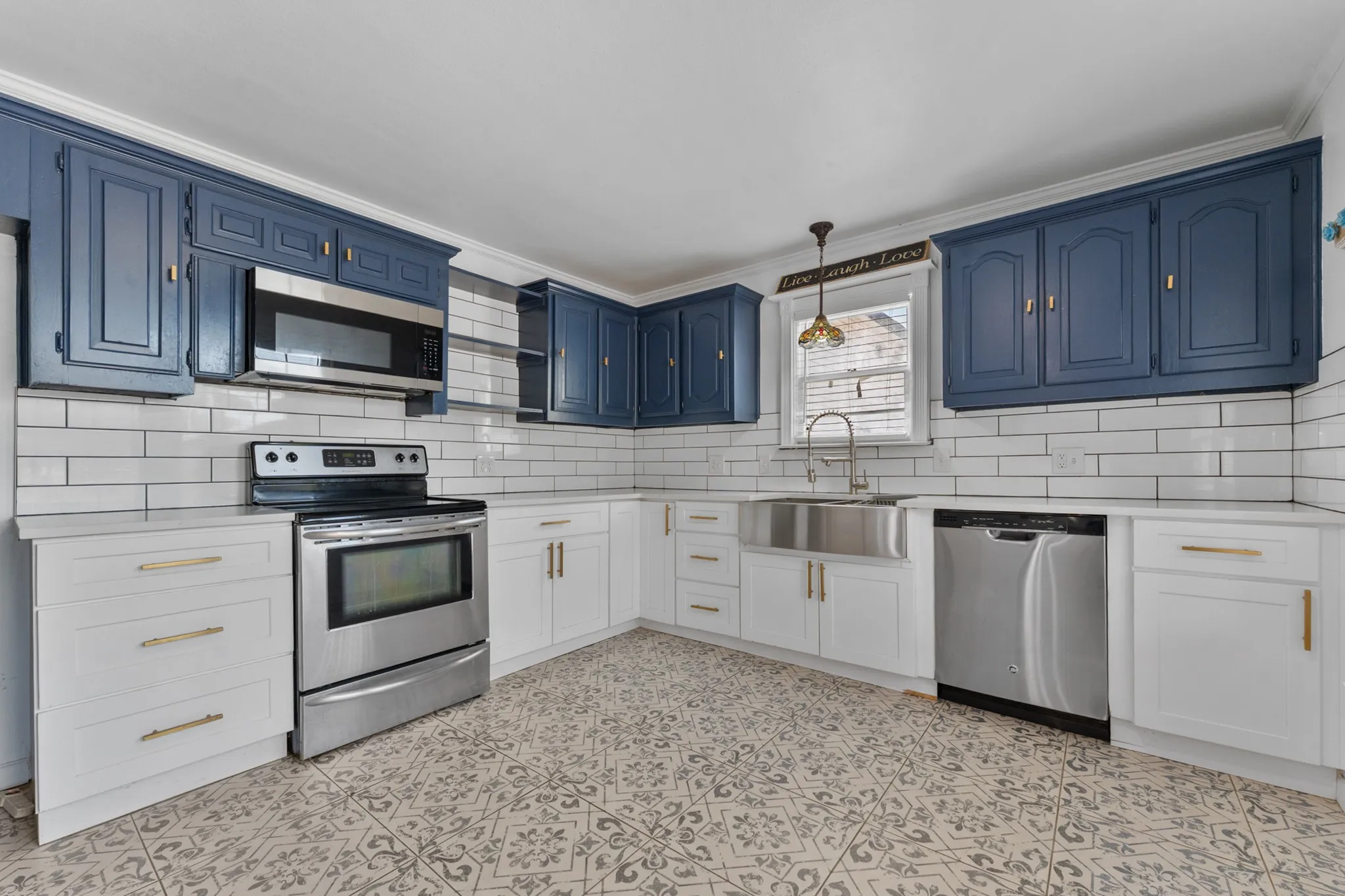 Kitchen featuring patterned tile flooring, stainless steel appliances, a farmhouse sink, white subway tile backsplash, and two-tone cabinetry