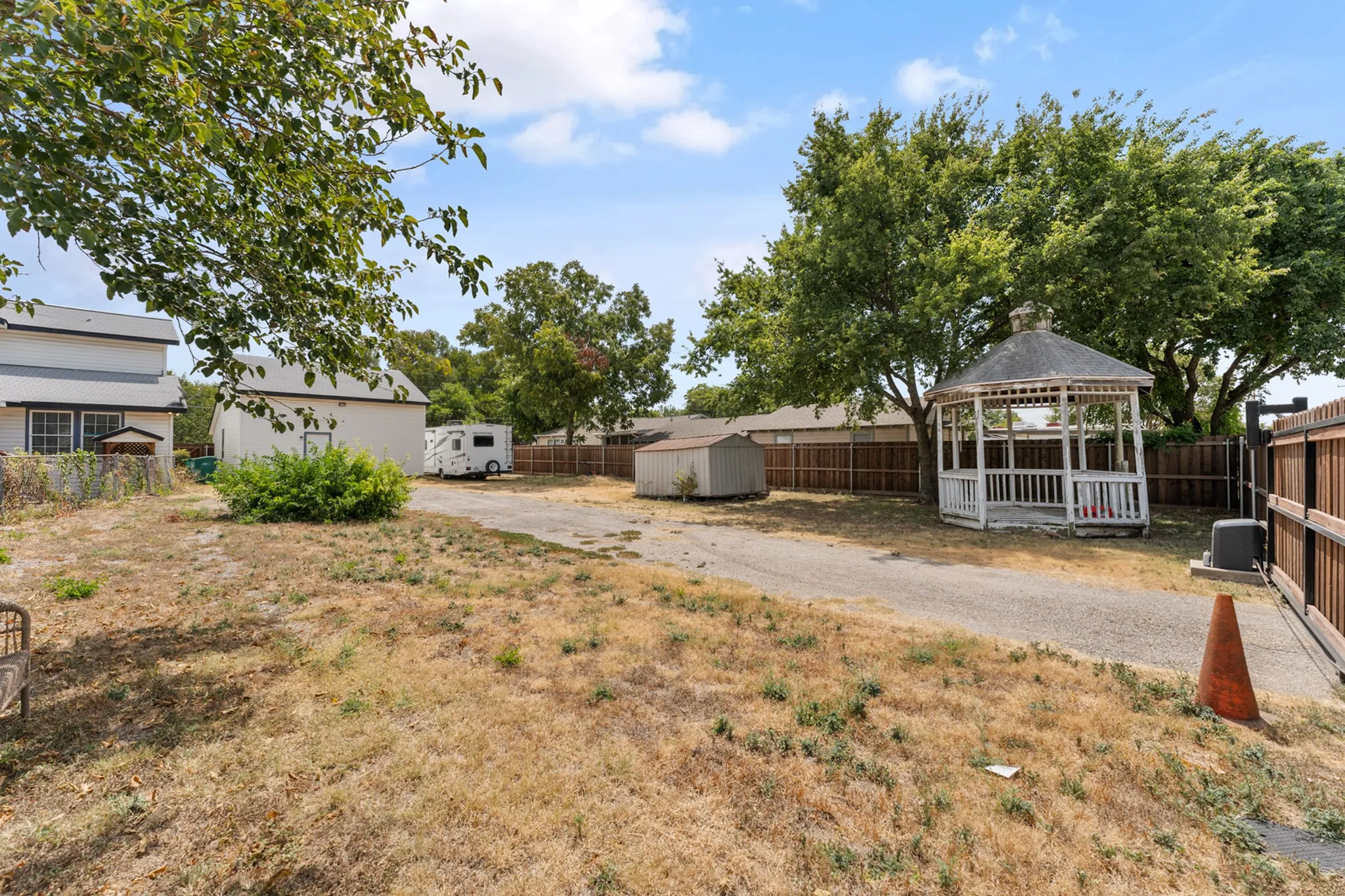 Expansive outdoor space featuring a paved driveway, detached storage shed, and a decorative gazebo