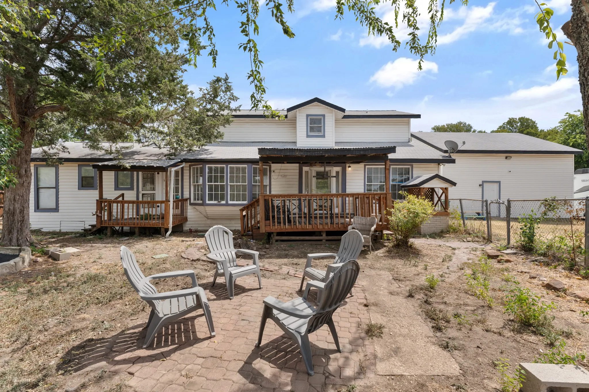 Rear exterior featuring multiple wood decks, a covered patio area, and a stone-paved section