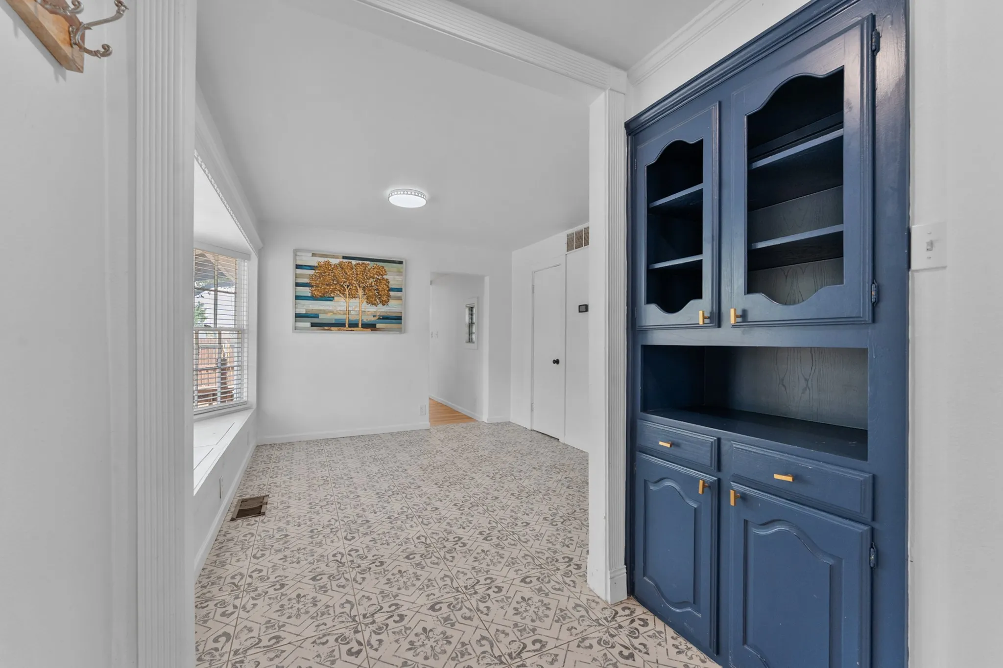 Built-in blue cabinetry with glass-front uppers, patterned floor tile, recessed lighting, and a window with blinds