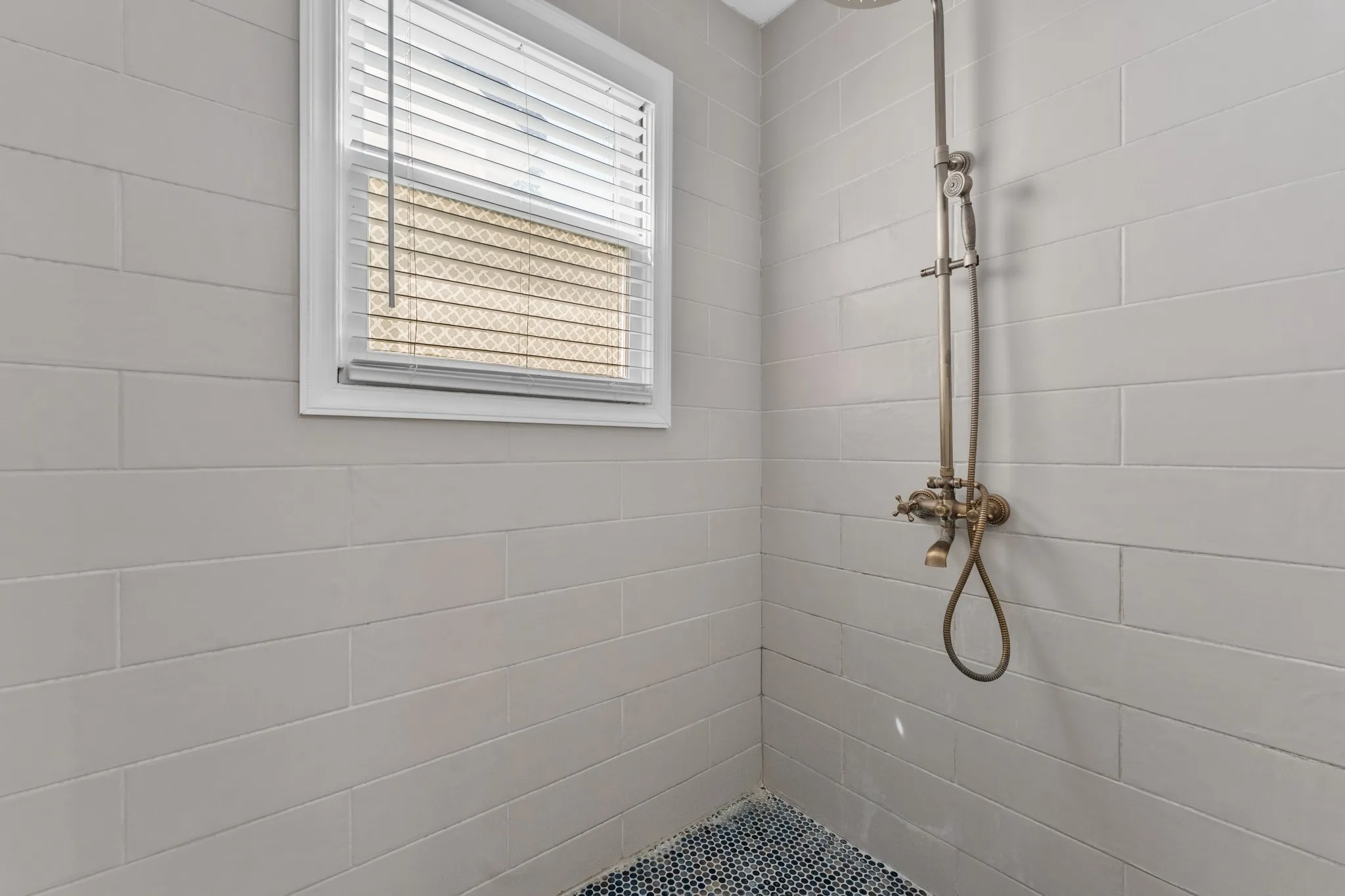 Subway tile shower surround with a window, complete with a vintage-style shower fixture and a mosaic tile floor