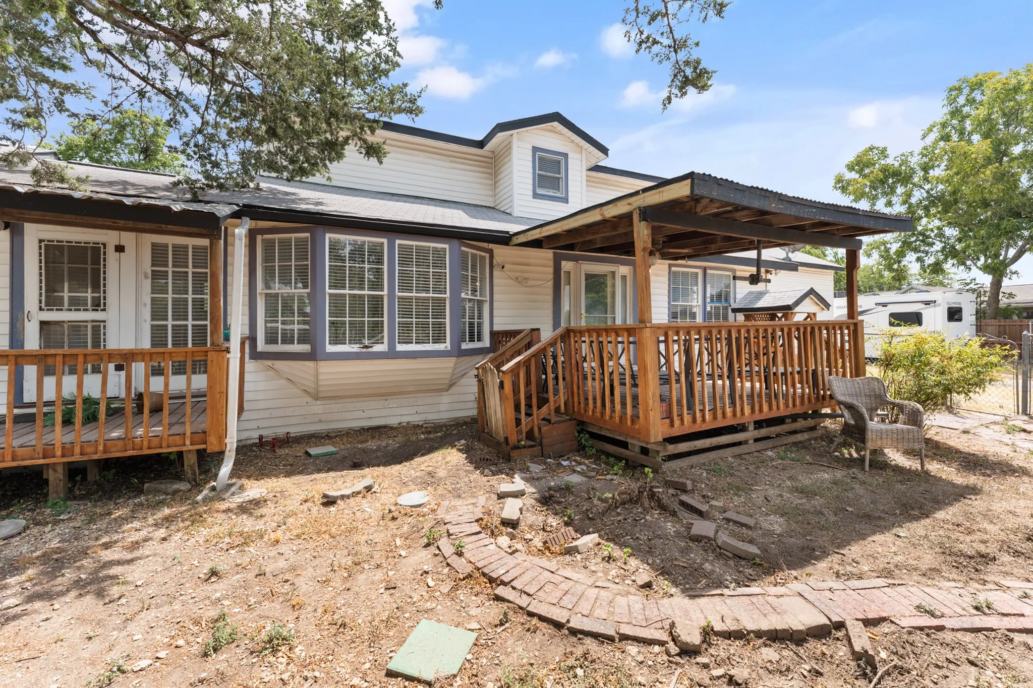 Rear exterior featuring an elevated wood deck with a covered patio, multiple windows, and a dormer