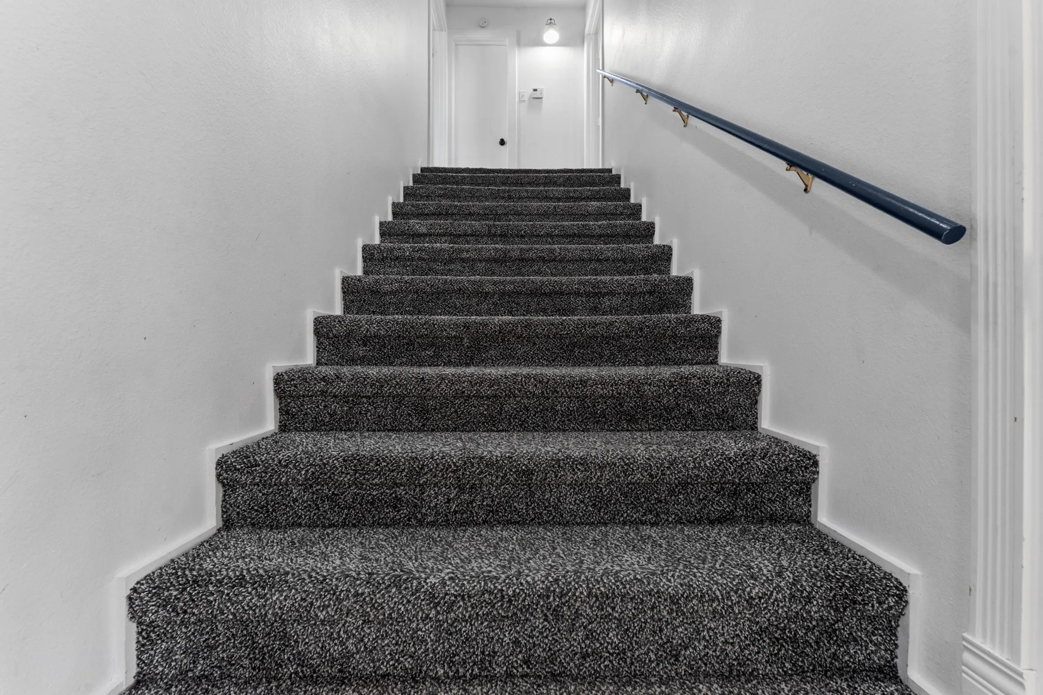 Staircase featuring dark gray carpeted treads and a dark-toned handrail