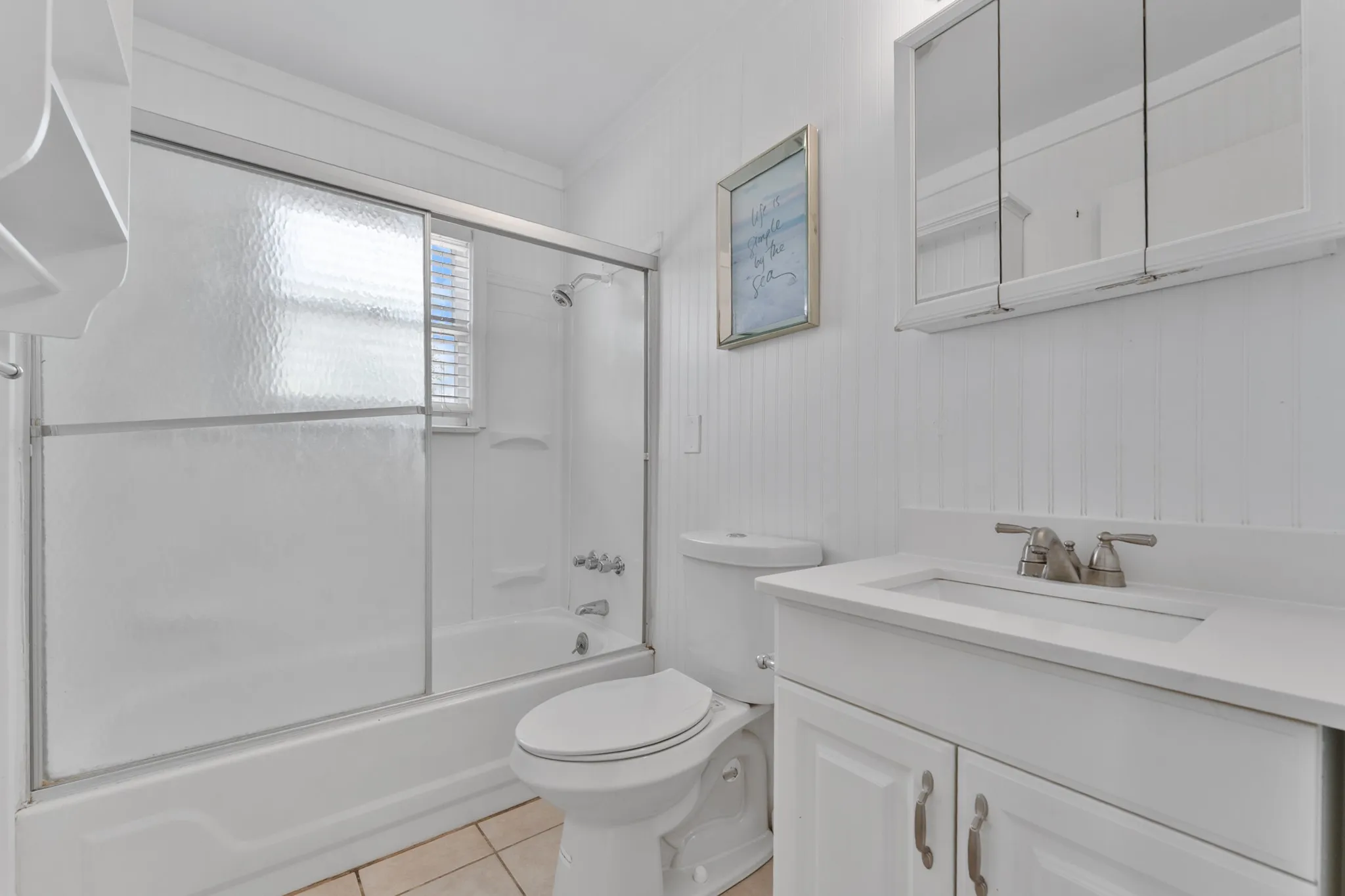 Built-in bathtub with sliding glass doors, white vanity with integrated sink, paneling wall treatment, and tiled flooring