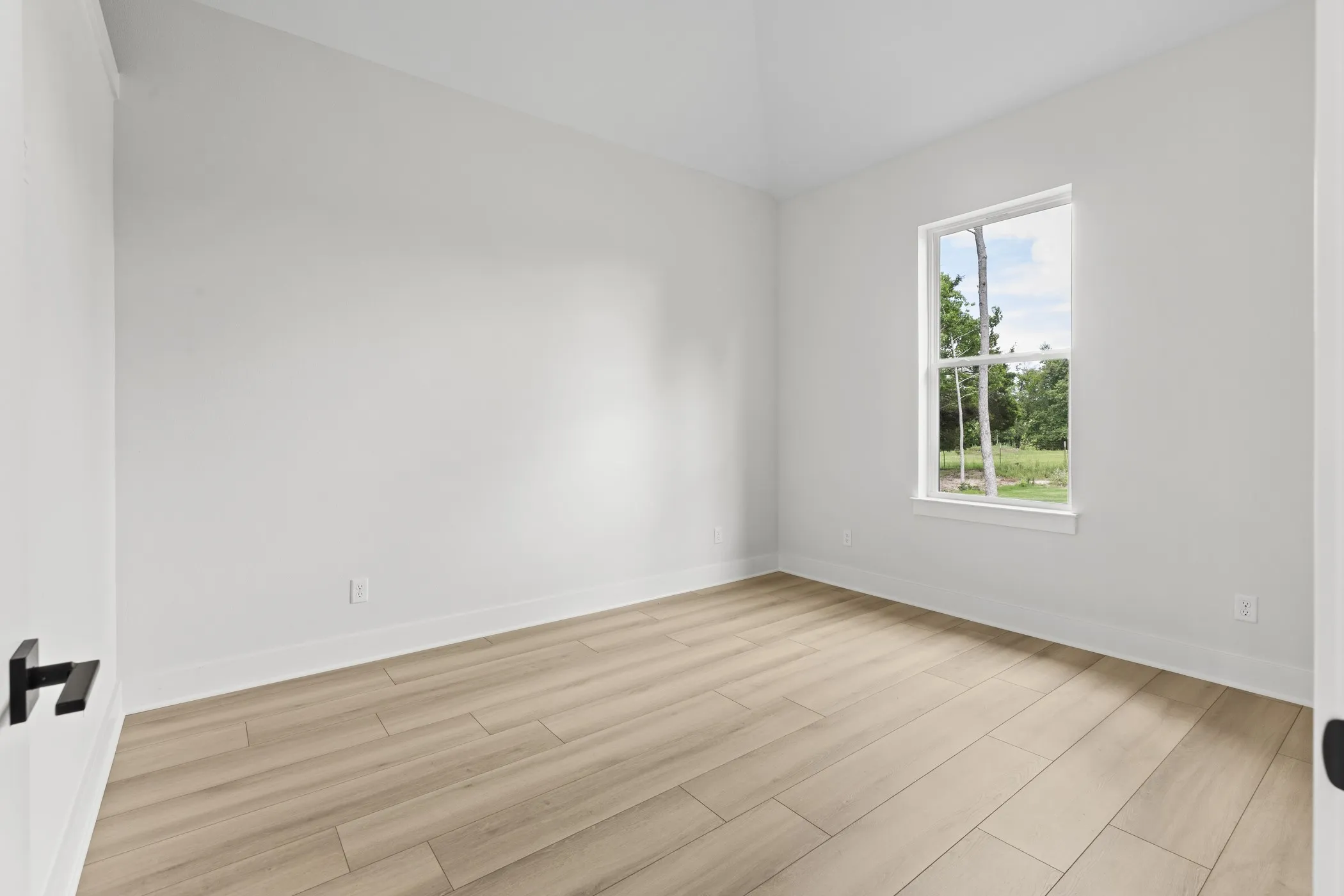 Neutral white walls, wood-finish flooring, and a single window with white trim