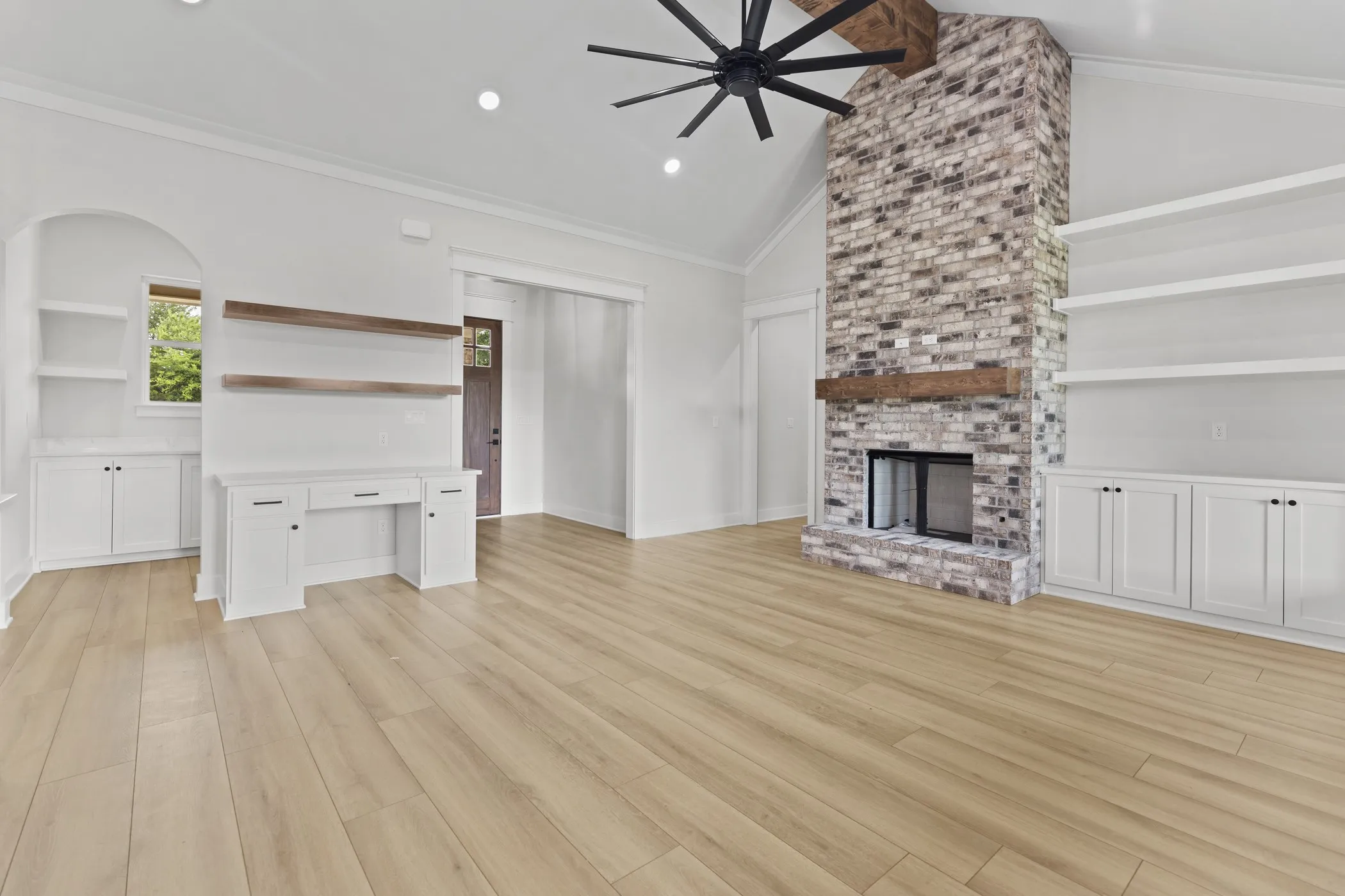 Vaulted ceiling with exposed wood beam, wood-finish flooring, floor-to-ceiling brick fireplace with wood mantel, built-in shelving, and recessed lighting