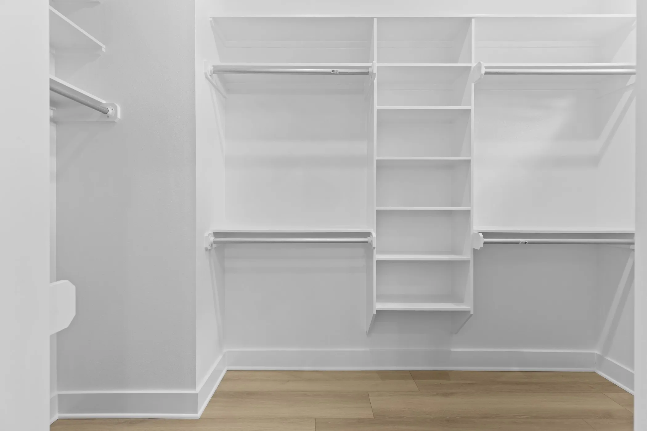Built-in closet shelving with multiple hanging rods and wood-finish flooring