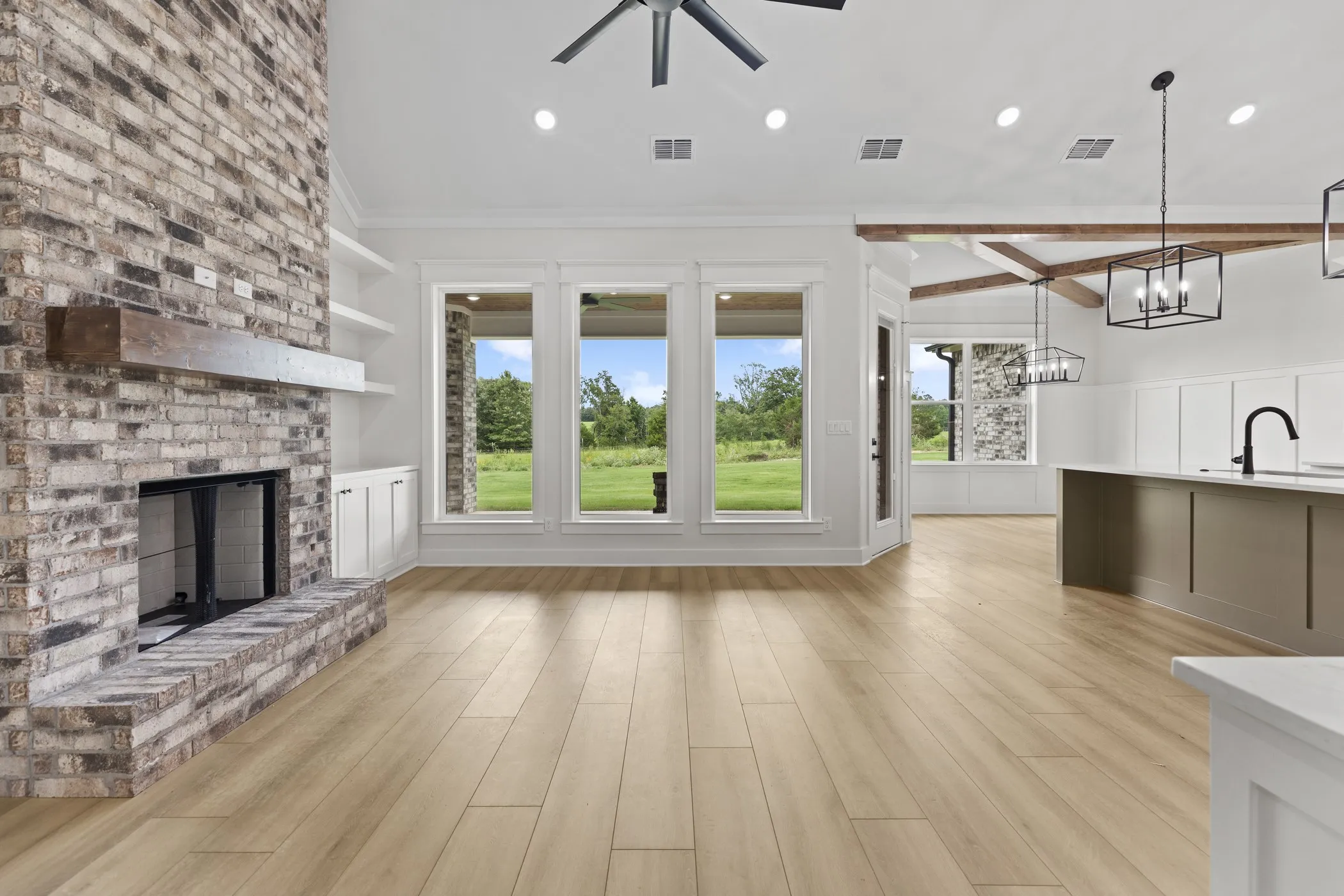 Brick-faced fireplace with a wood mantel, built-in shelving, wood-finish flooring, and exposed ceiling beams