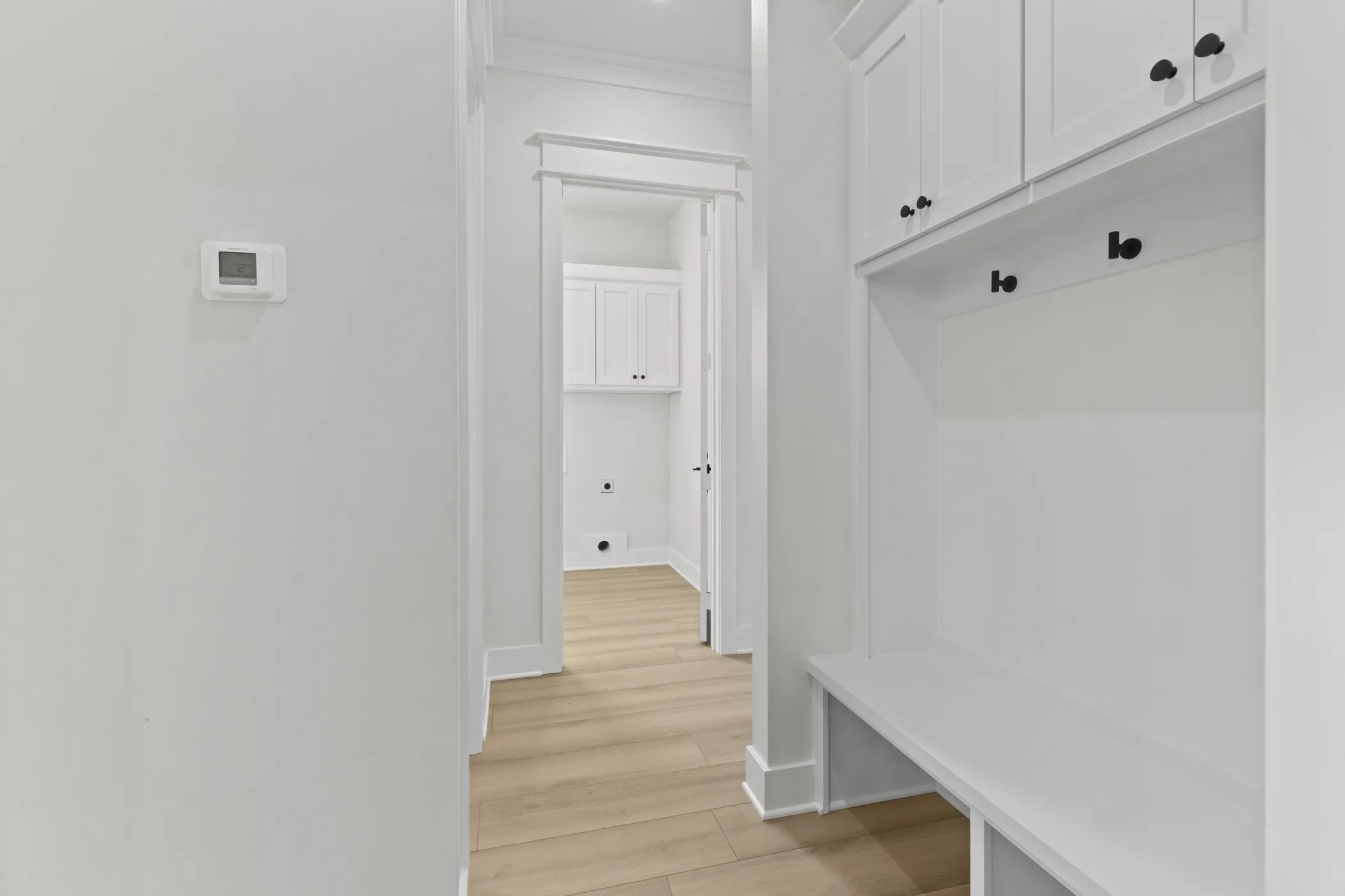 Built-in storage bench with overhead cabinetry and matte black hardware, wood-finish flooring, and crown molding