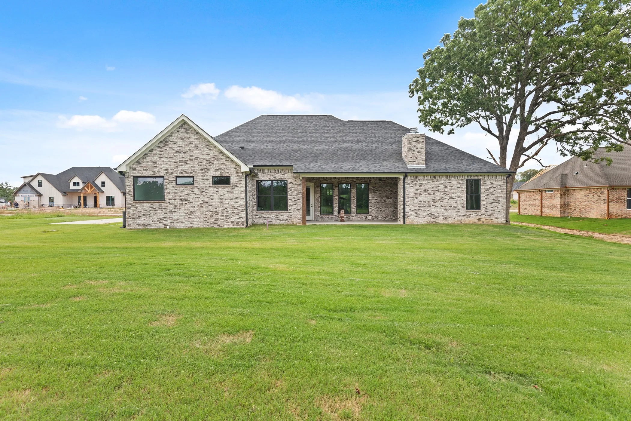 Expansive backyard with a manicured lawn, brick exterior, covered patio, and large windows