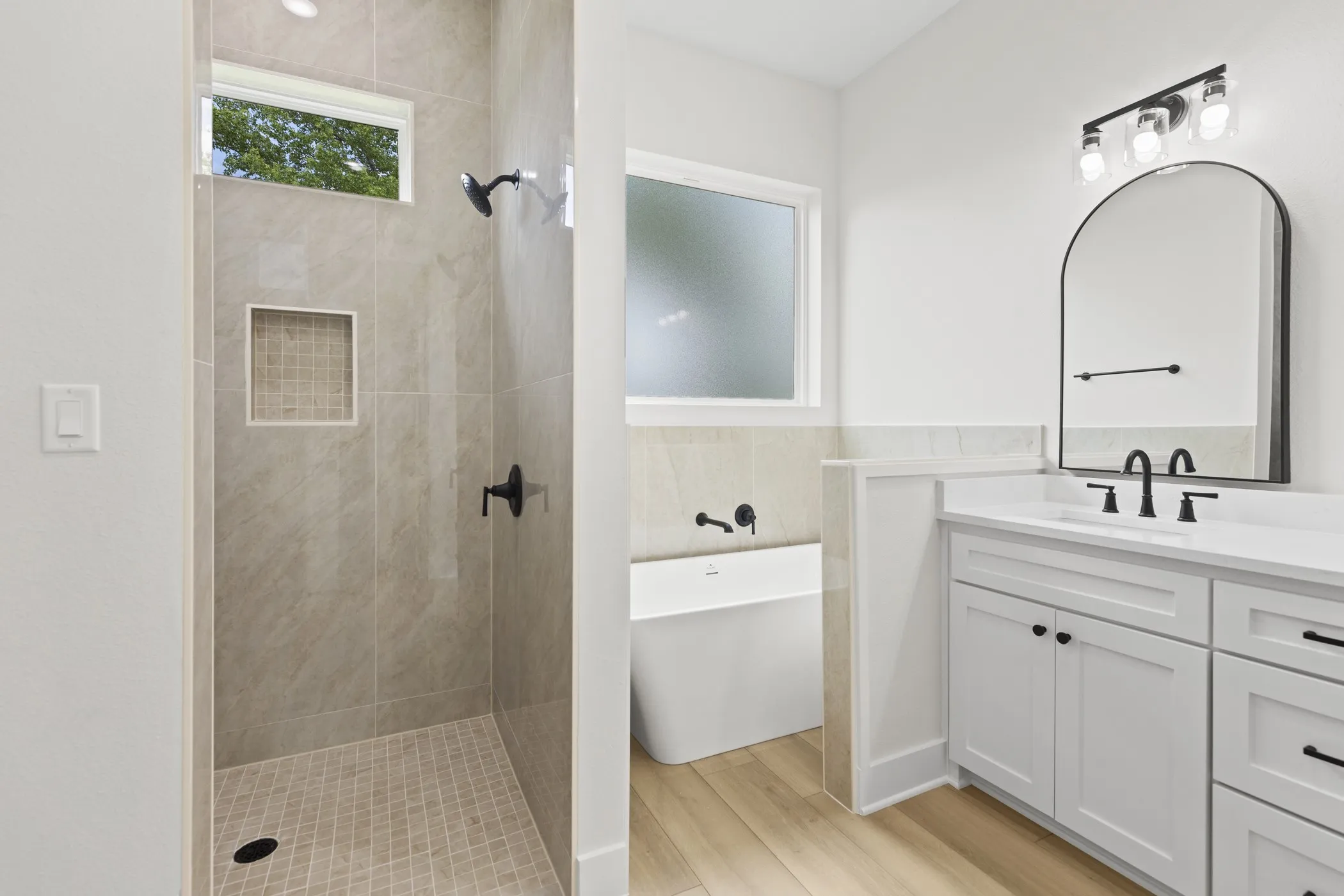 Tiled shower with a niche, freestanding tub, dual-sink vanity with white cabinetry, and wood-finish flooring