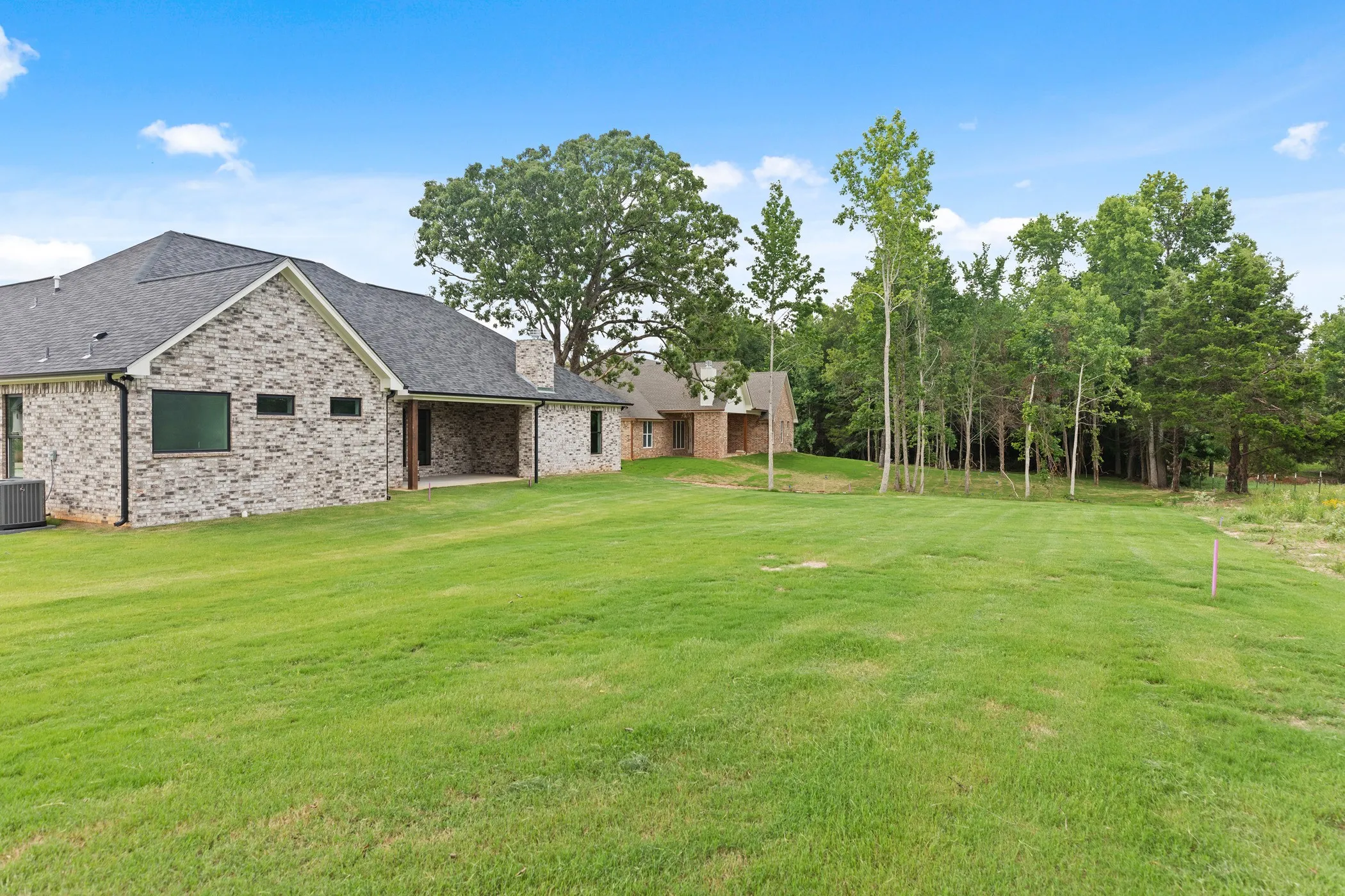 Expansive lawn with mature trees and a brick exterior home featuring a covered patio