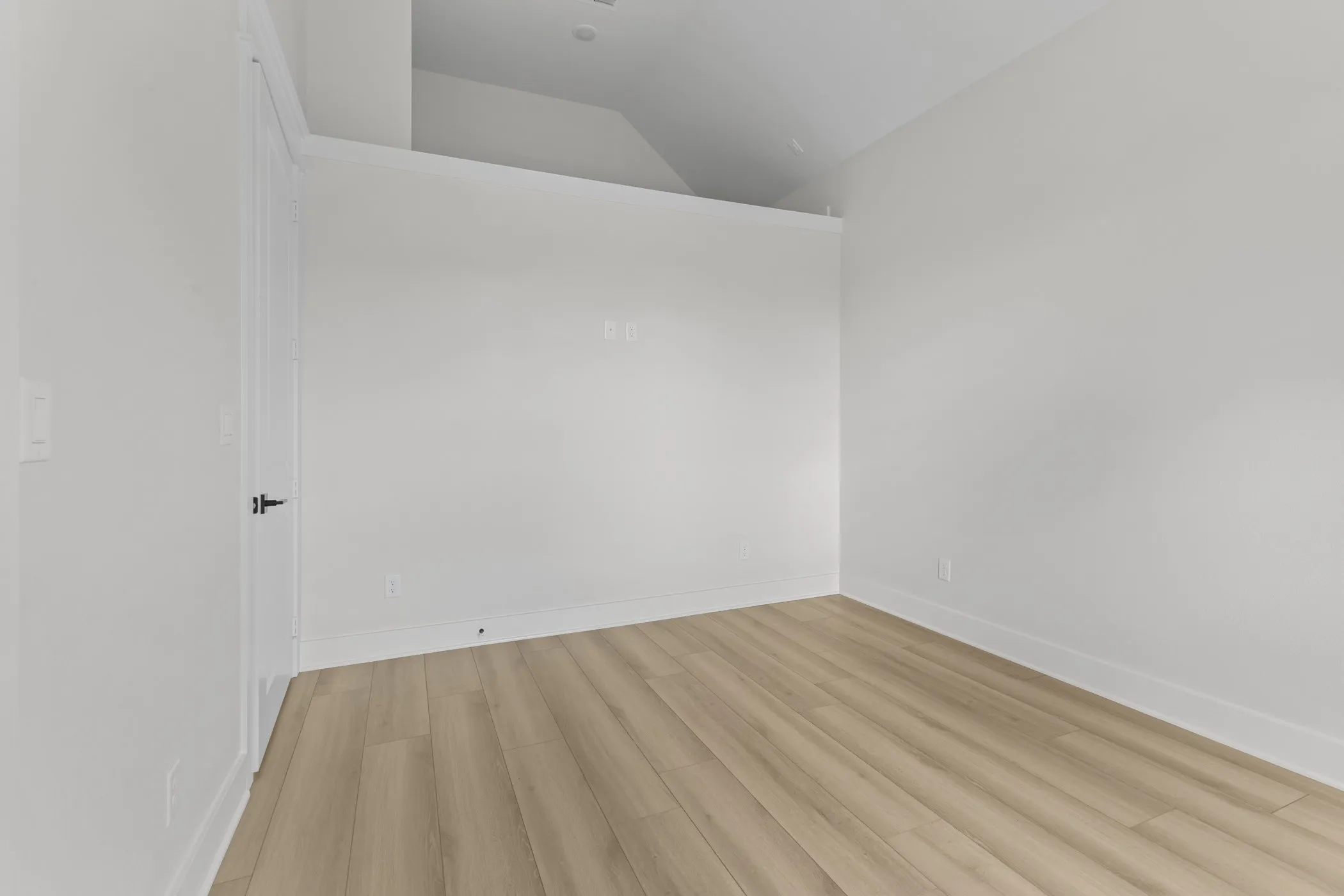 Recessed lighting, light wood-finish flooring, white walls, white trim, and a white interior door with black hardware