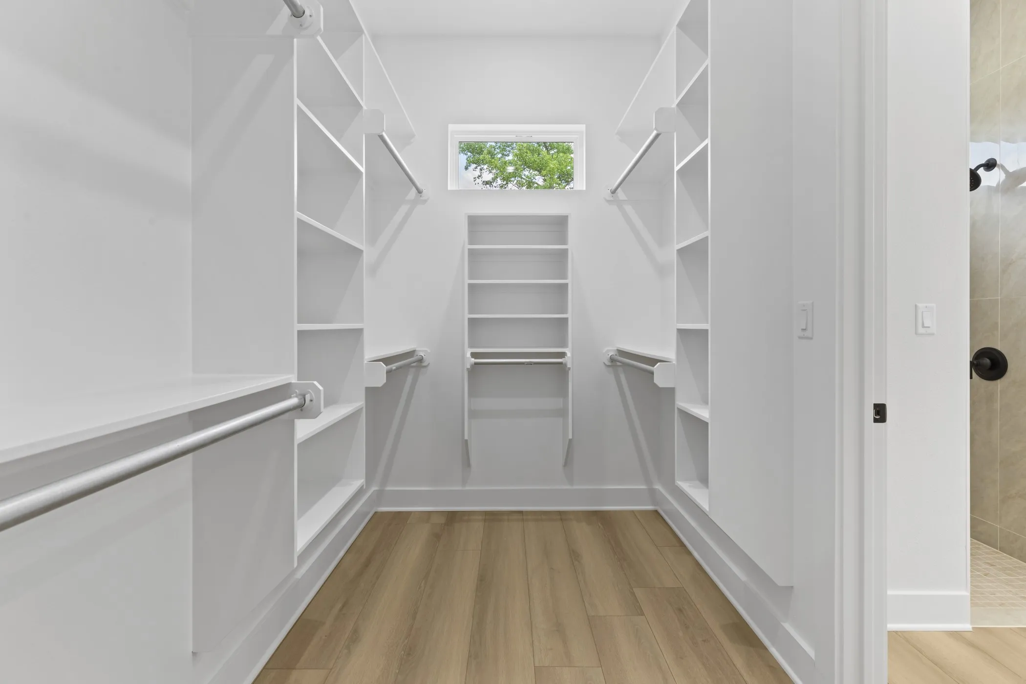 Walk-in closet with extensive built-in shelving, multiple hanging rods, wood-finish flooring, and a transom window
