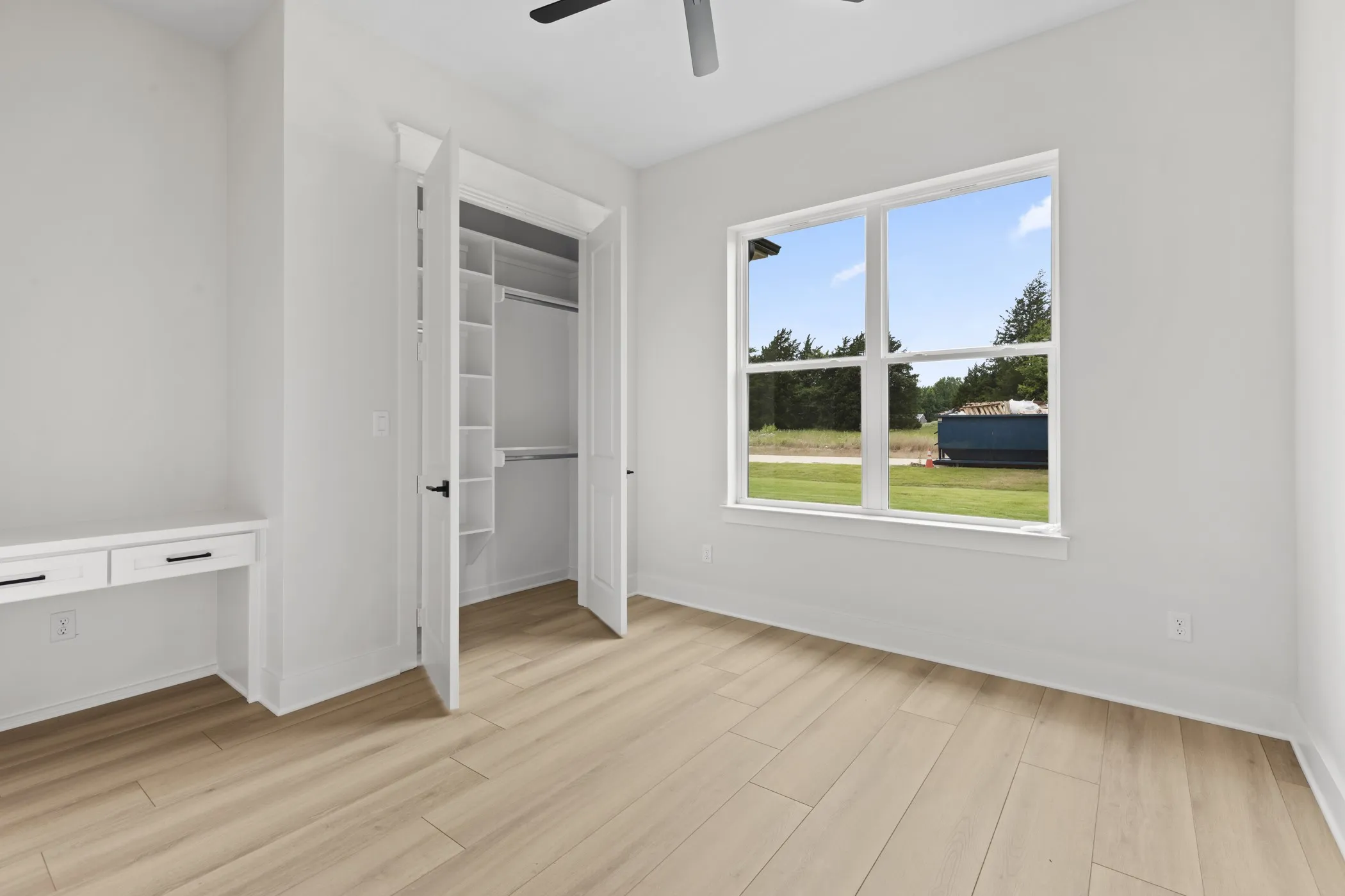 Wood-finish flooring, built-in desk with drawers, built-in closet shelving, ceiling fan, and large window