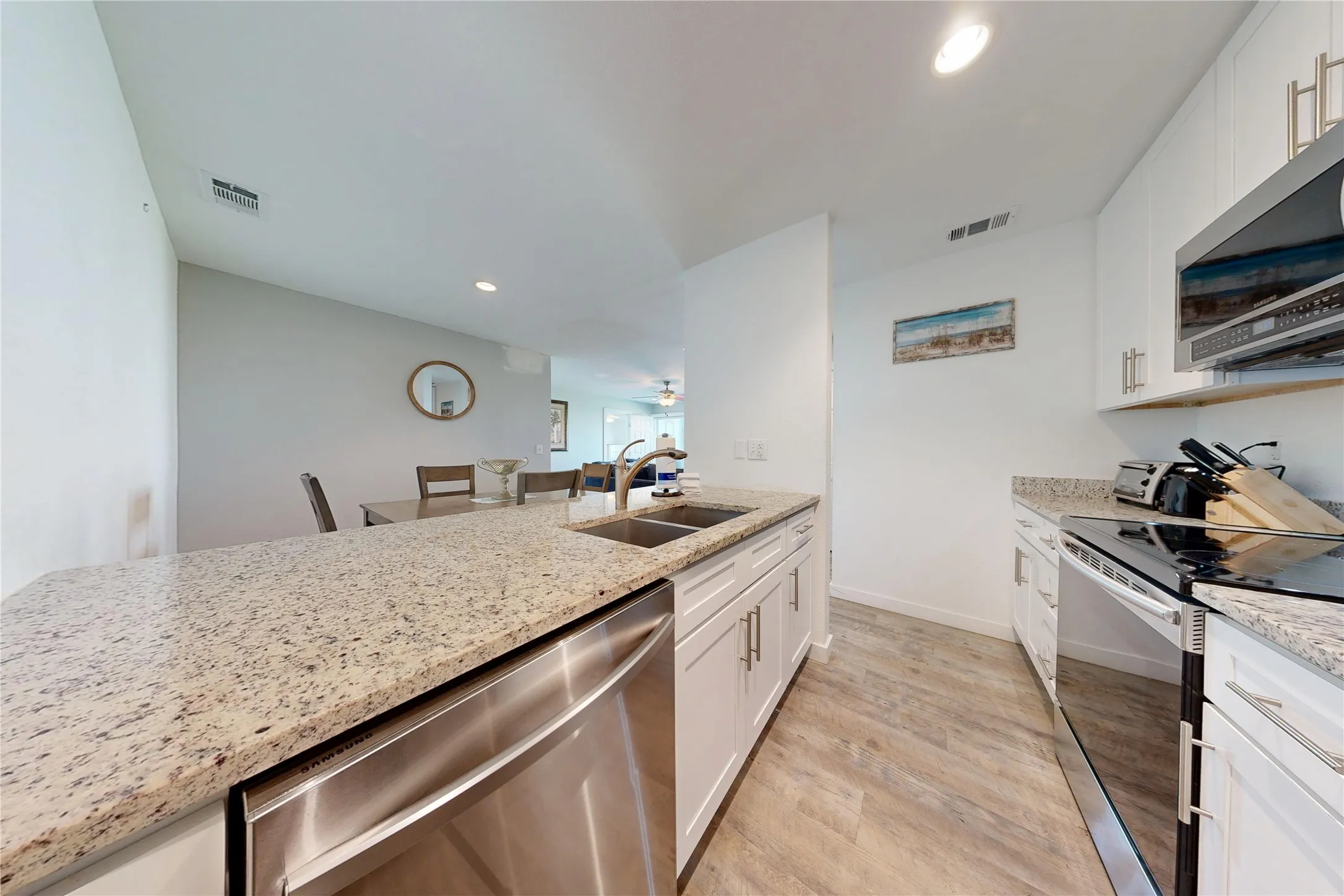Kitchen featuring granite countertops, stainless steel appliances, white cabinetry with silver hardware, an undermount sink, and wood-finish flooring