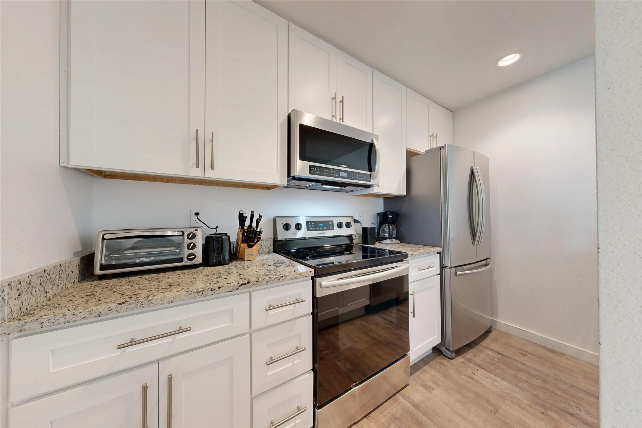 White cabinetry with stainless steel hardware, granite-style countertops, stainless steel appliances, and wood-finish flooring